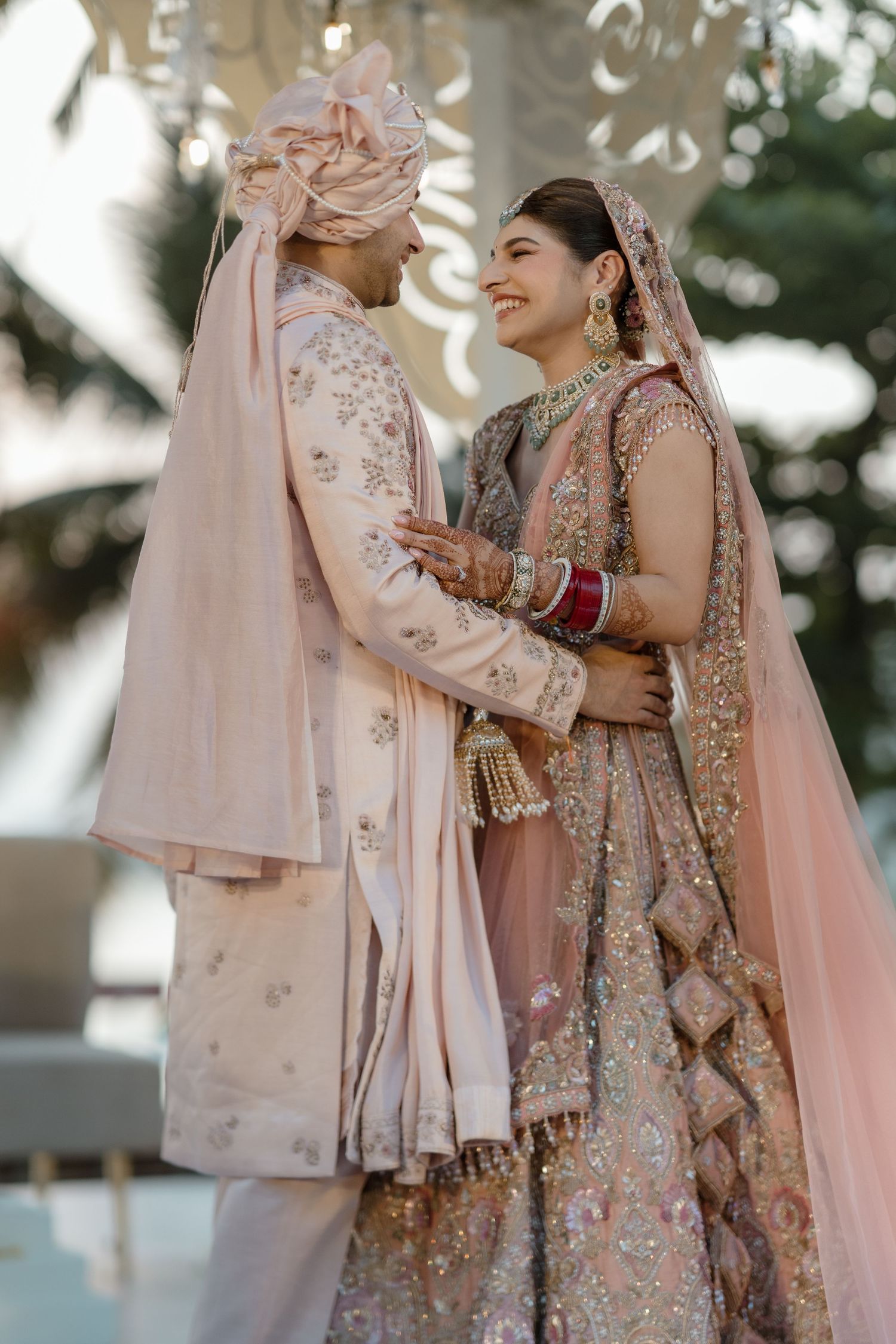 Traditional Indian wedding couple wearing elegant pink and gold embroidered outfits during their outdoor ceremony.
