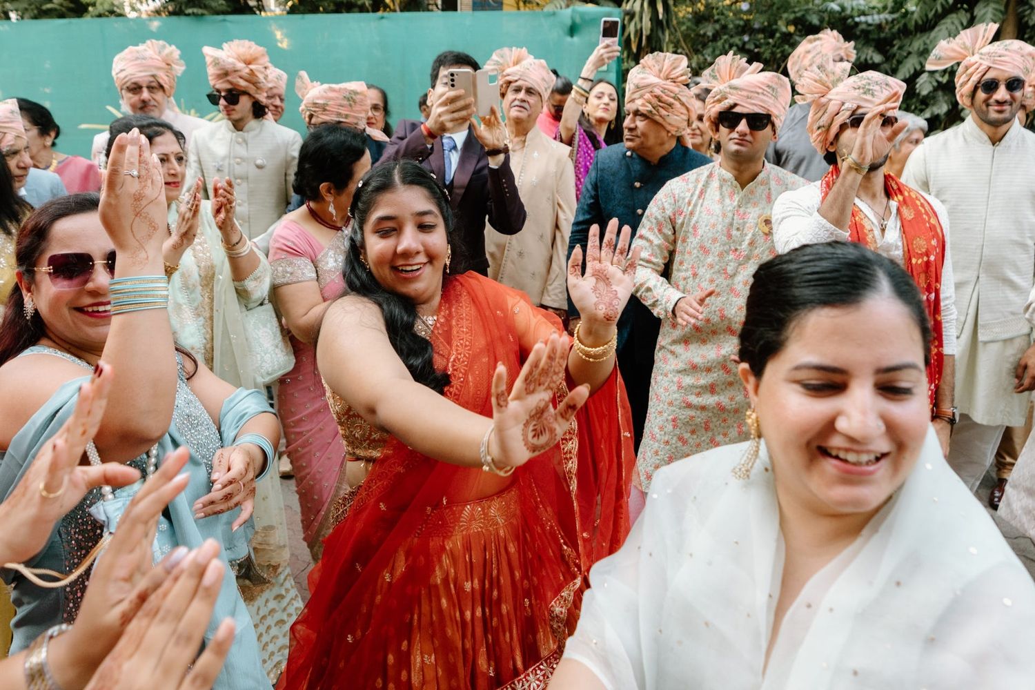 Wedding guests dance and celebrate joyfully during an outdoor celebration in traditional Indian and Western attire.