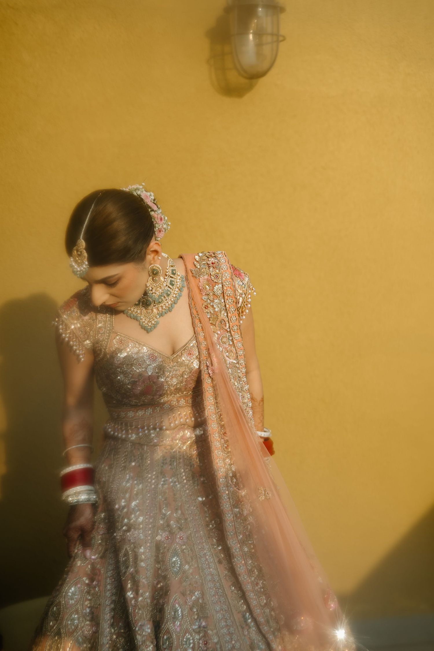 A detailed shot of an ornate silver and peach lehenga with intricate beadwork and flowing dupatta against a yellow wall.