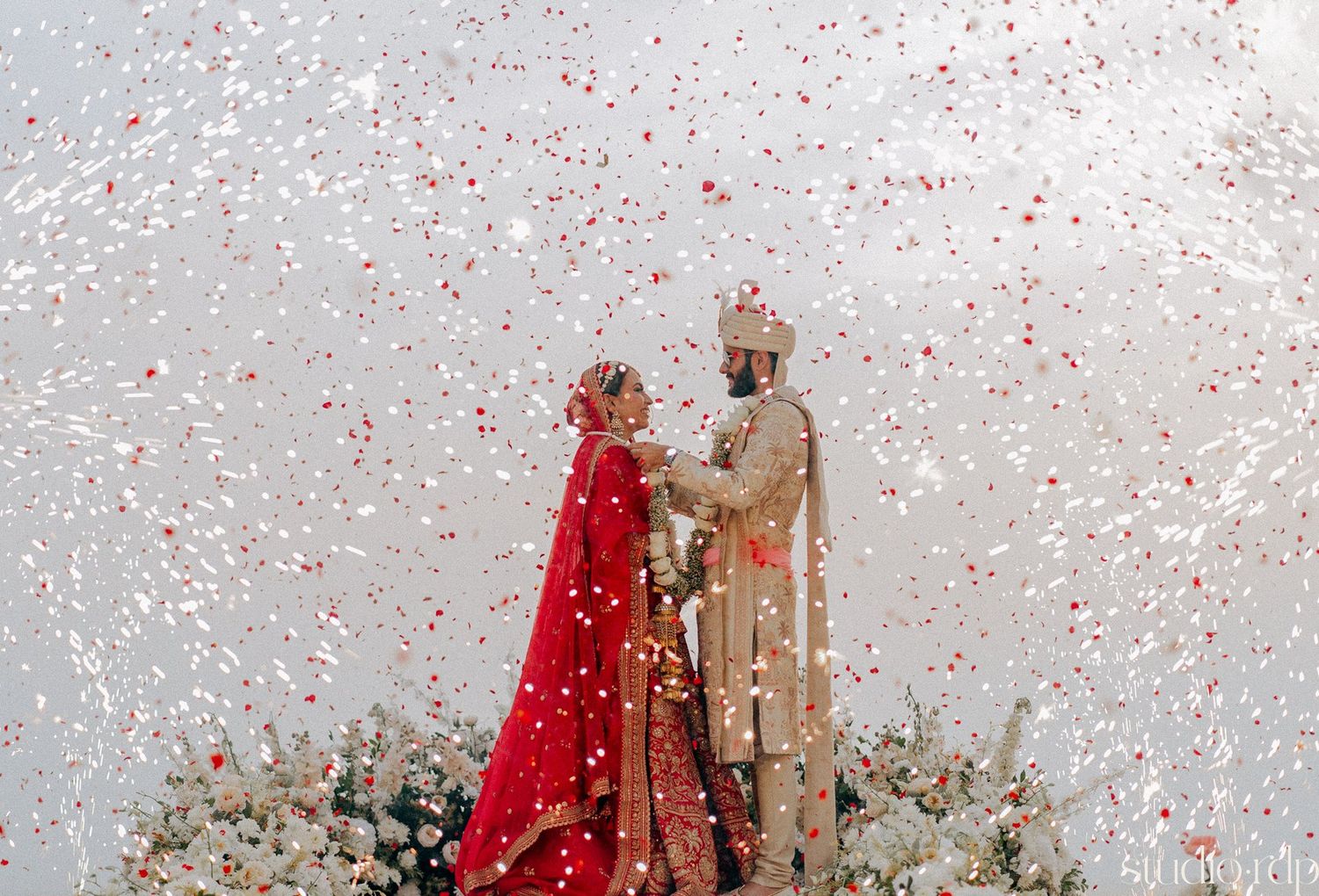 Festive wedding celebration with confetti and traditional attire at an outdoor venue.