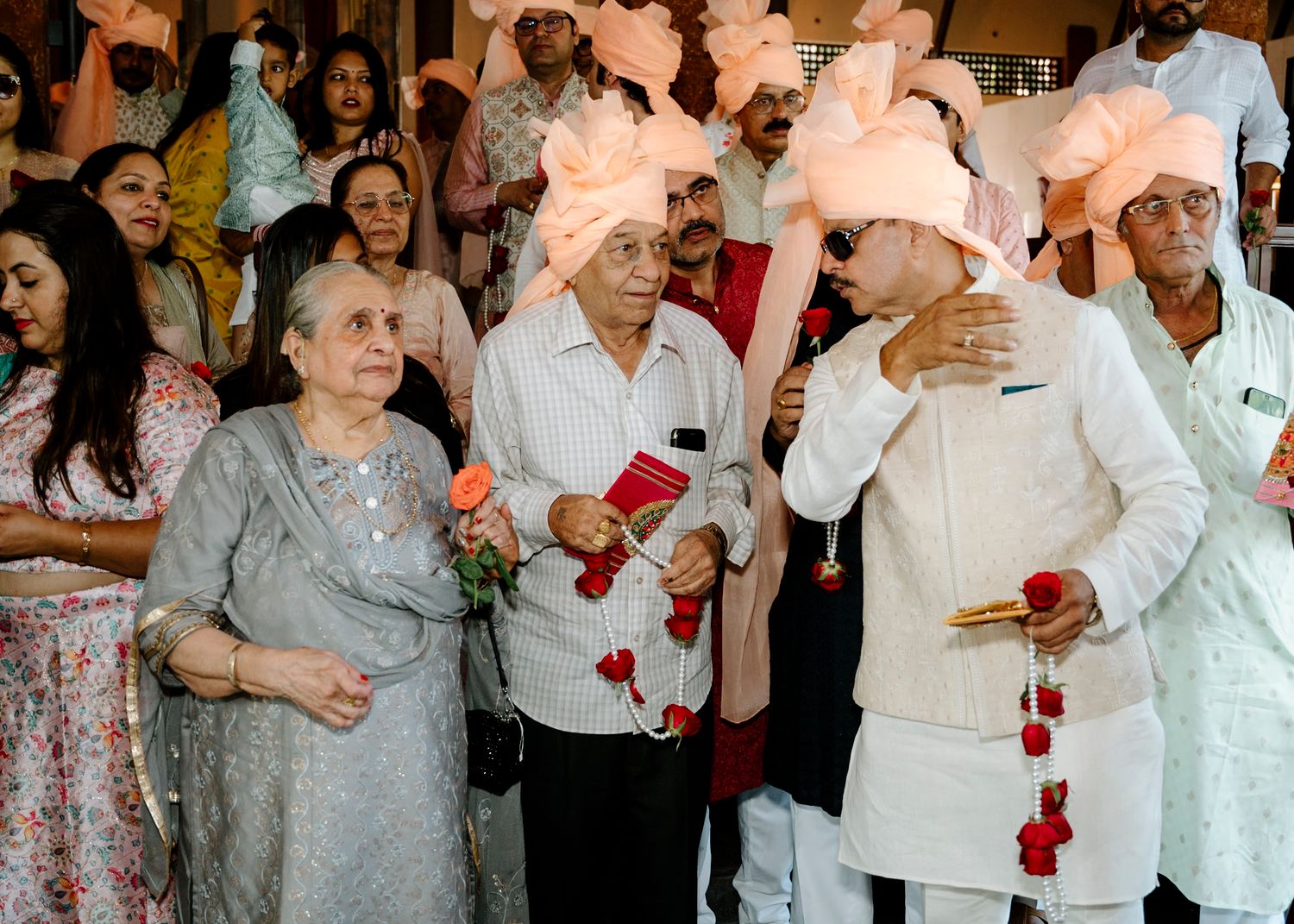 Wedding guests in formal attire scattering rose petals during celebration.