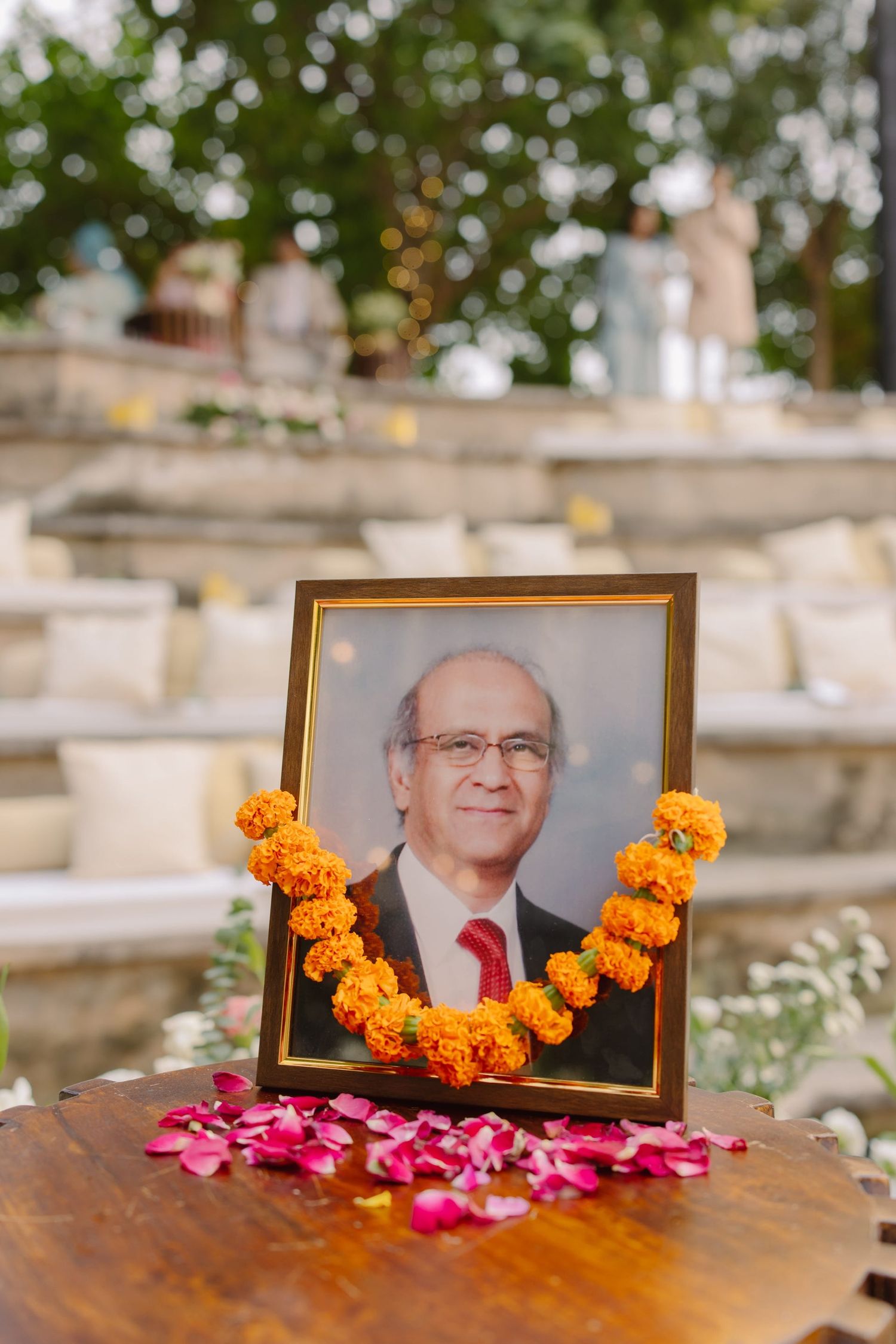 A memorial photo display with marigold garlands and scattered rose petals.