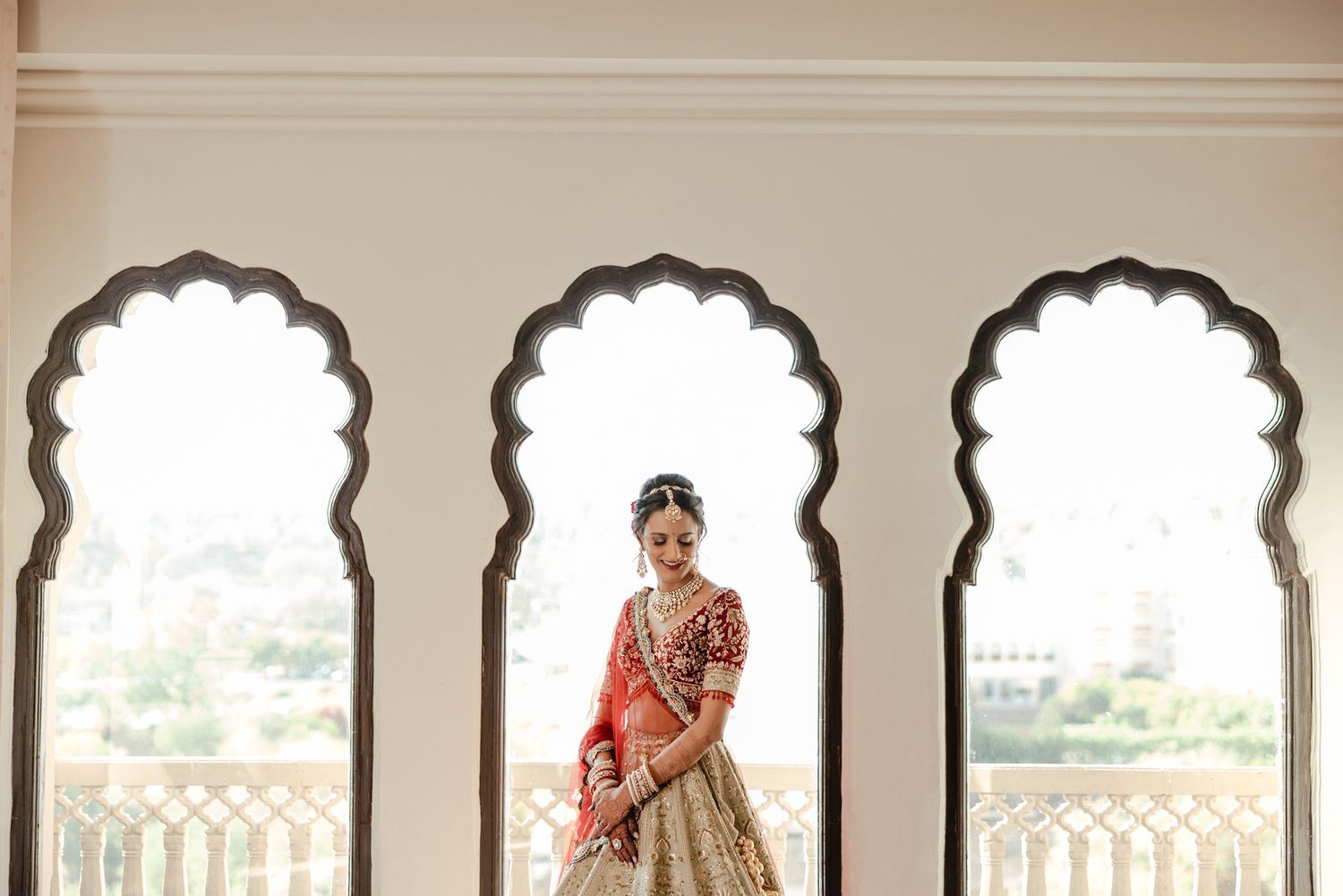 Traditional Indian bridal attire is showcased through ornate arches at an elegant venue with scenic views.