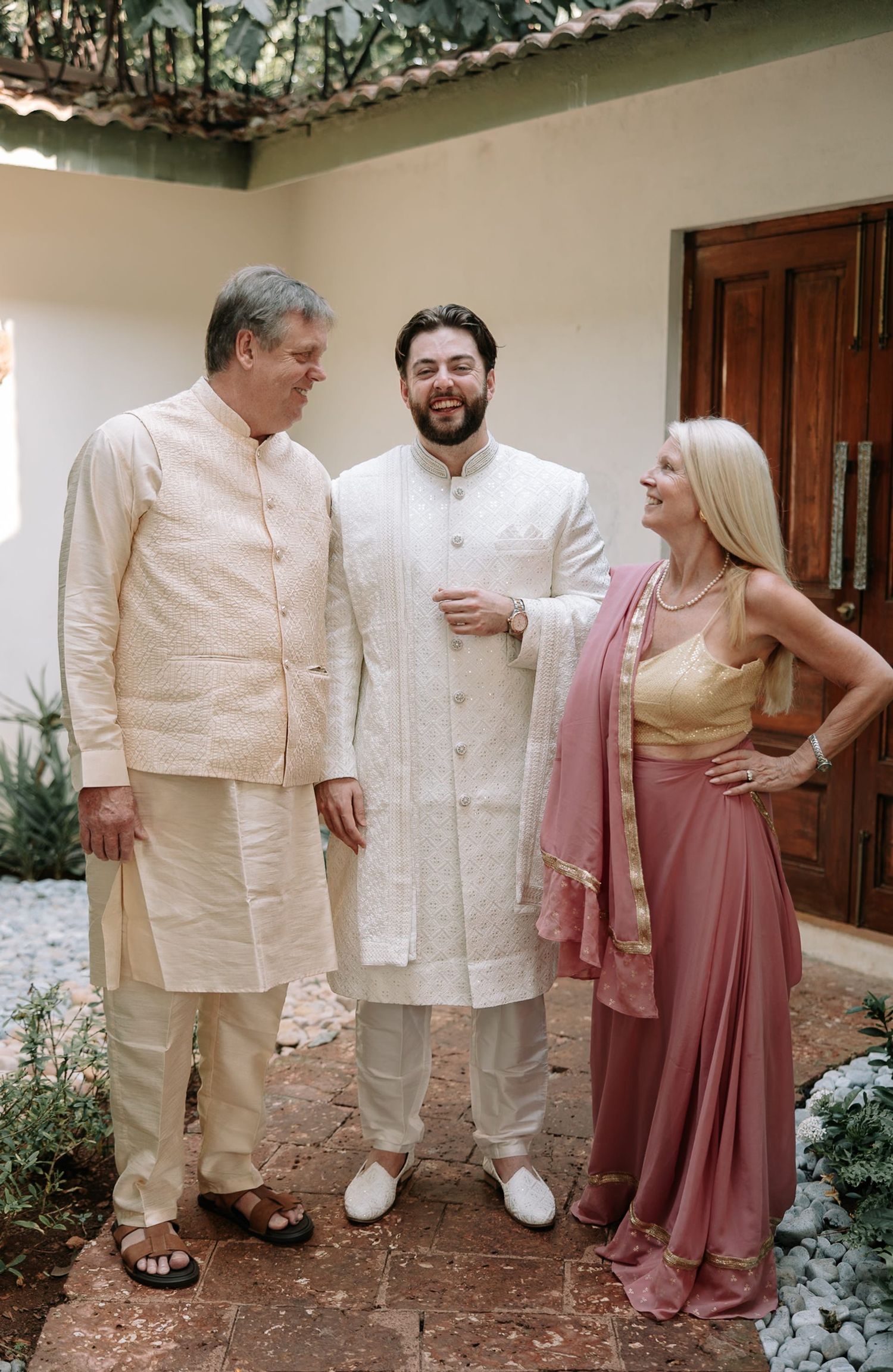 Three people in traditional South Asian attire pose together outdoors at a wedding celebration.
