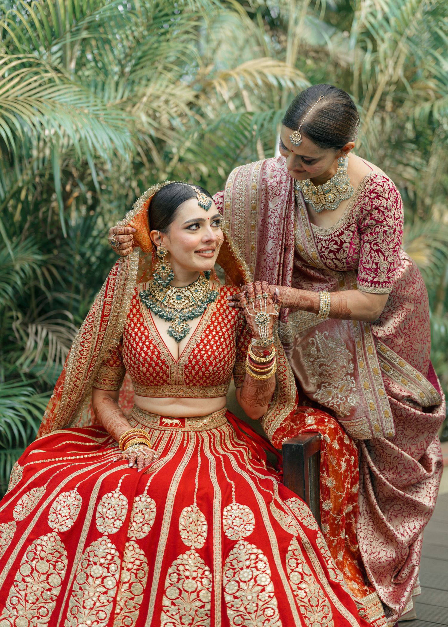 Traditional Indian bridal outfit in red and gold with detailed embroidery and rich embellishments captured in natural setting.