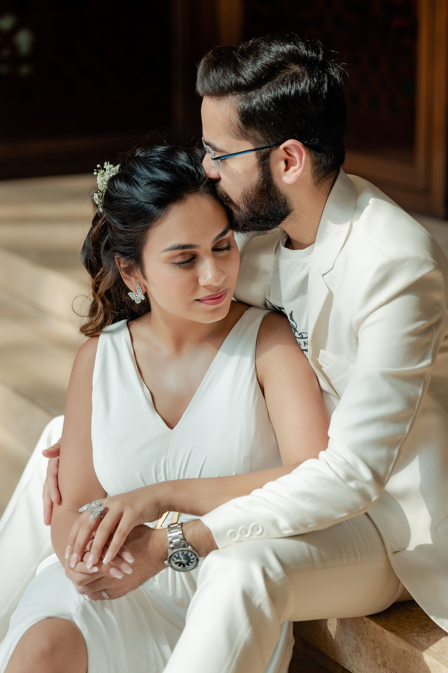 Intimate portrait of couple in white attire sitting in warm sunlit interior.