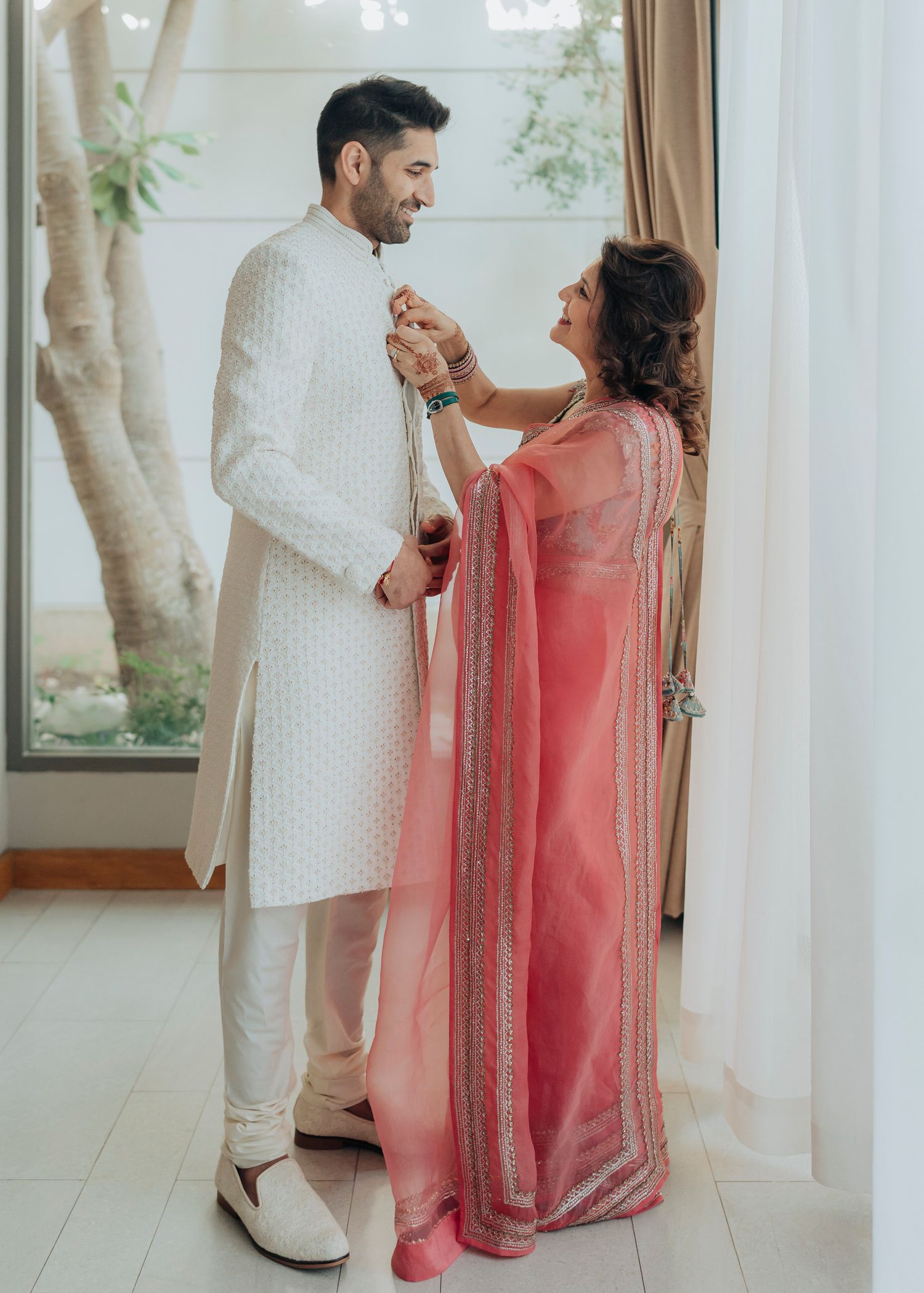 A couple in traditional Indian attire shares a playful moment as they laugh and interact in a sunlit room.
