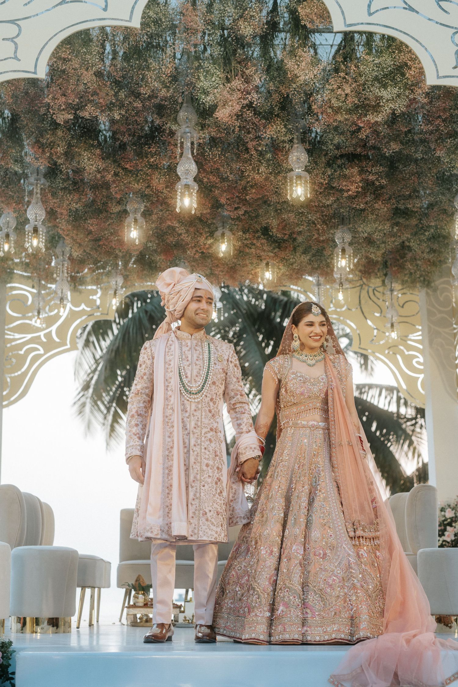 Elegant pink and gold embellished South Asian wedding lehengas displayed under a gazebo with hanging lights.