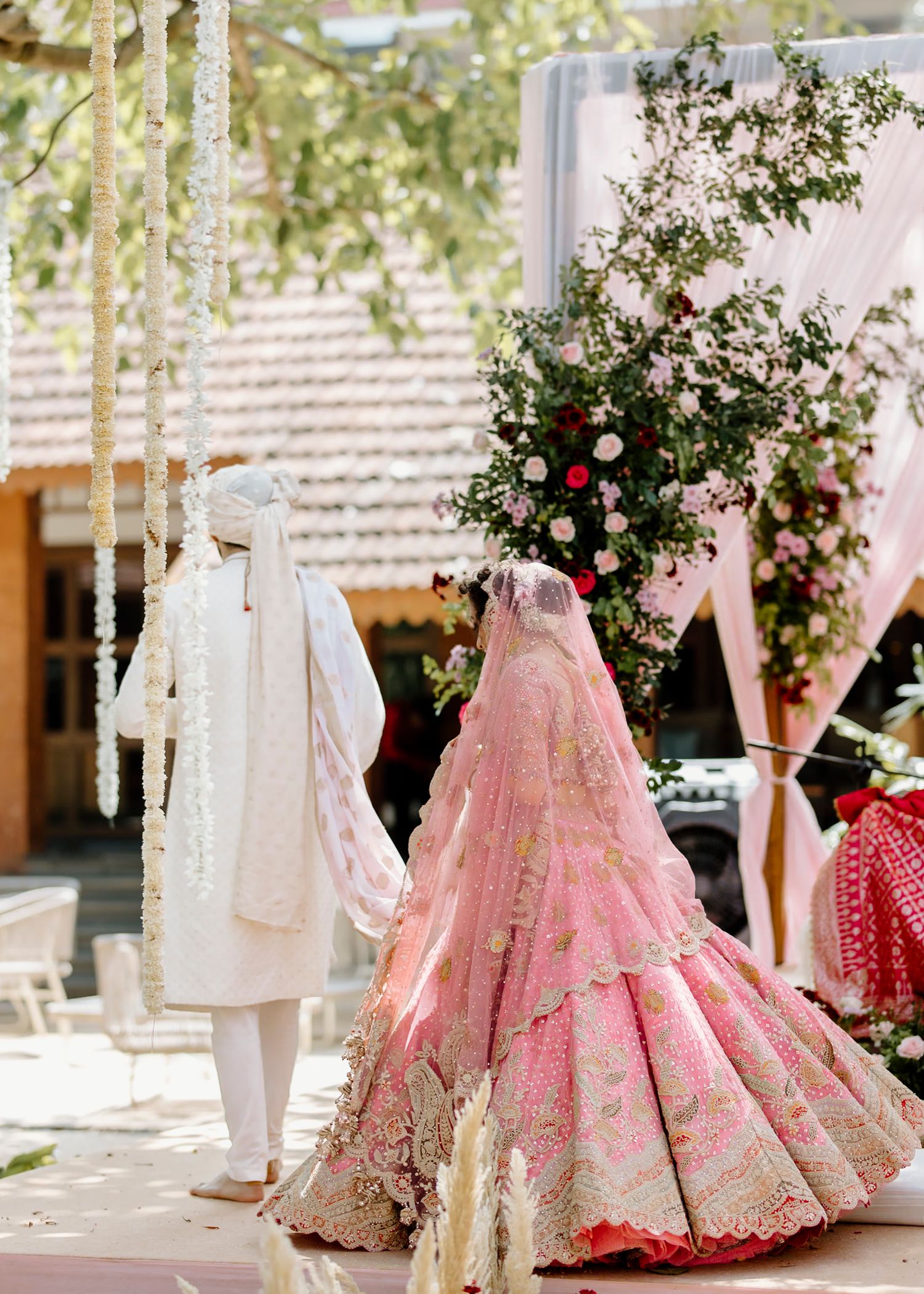 Wedding venue decorated with pink lehengas and white traditional outfits under trees.