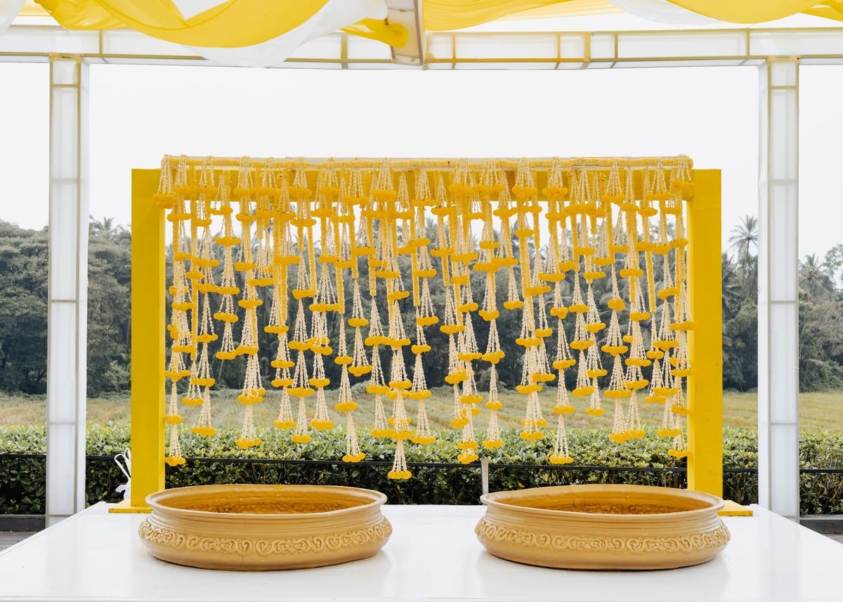 Yellow backdrop with hanging floral decorations between white pillars outdoors.