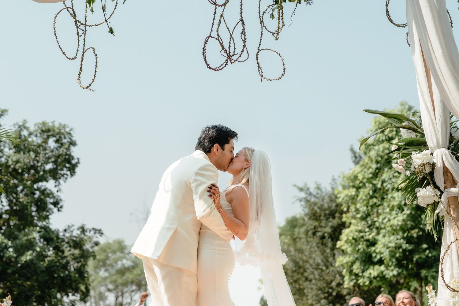 Wedding couple sharing intimate moment under hanging decorations and white draped canopy.