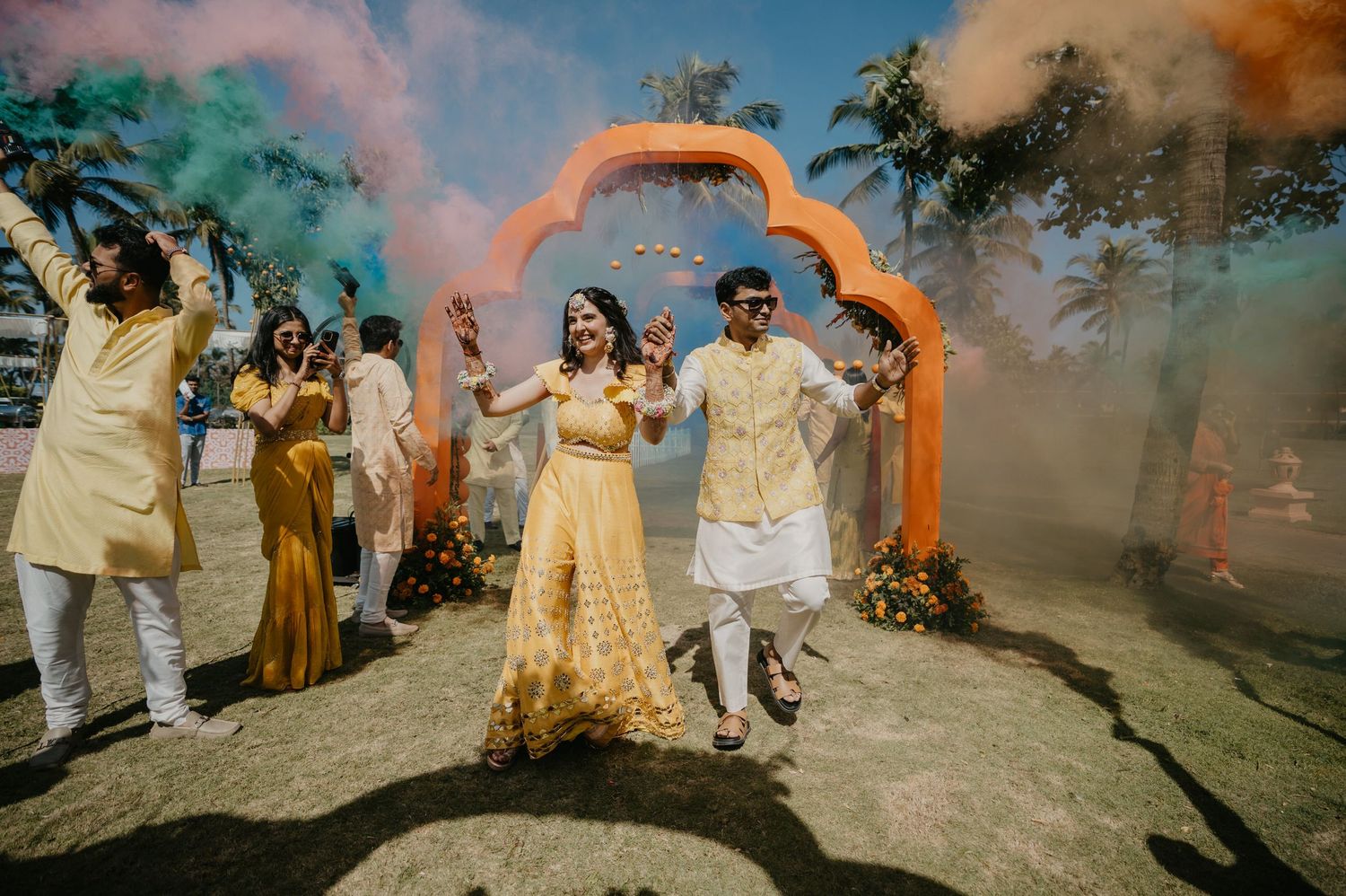 Wedding celebration with colorful smoke bombs and archway as couple dances during outdoor ceremony festivities.