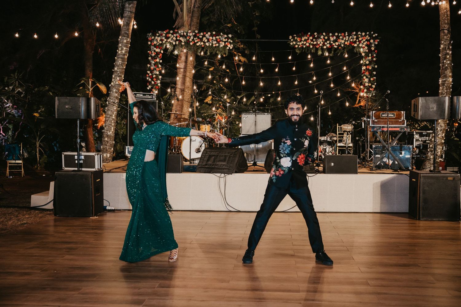 Couple dancing elegantly at an outdoor evening wedding reception with string lights and a stage in the background.