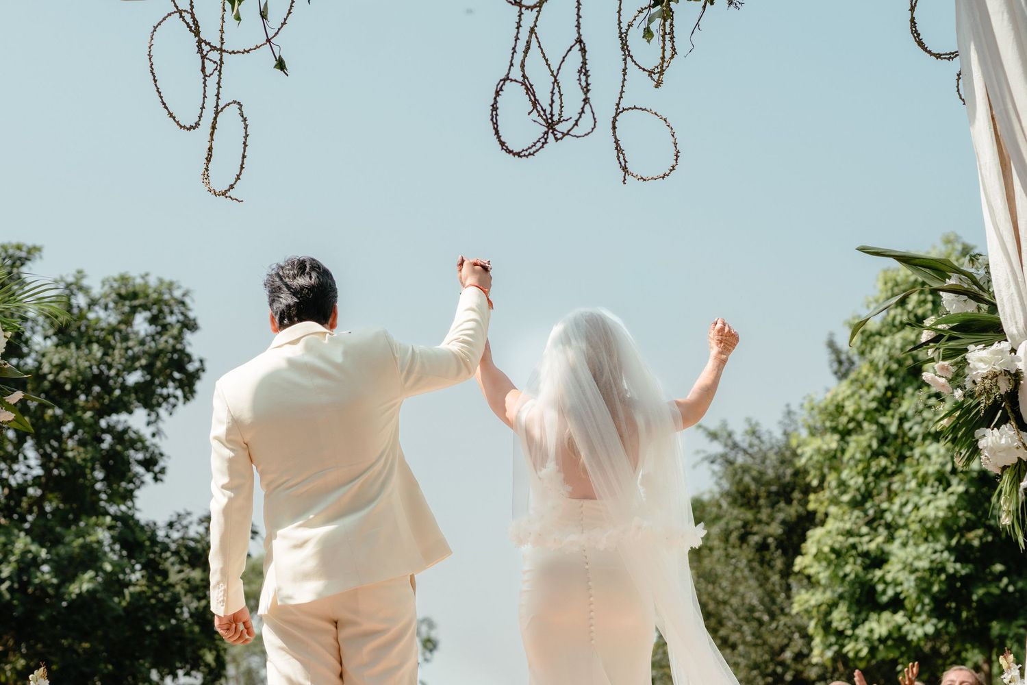 Celebratory moment with couple raising hands under outdoor wedding decor.