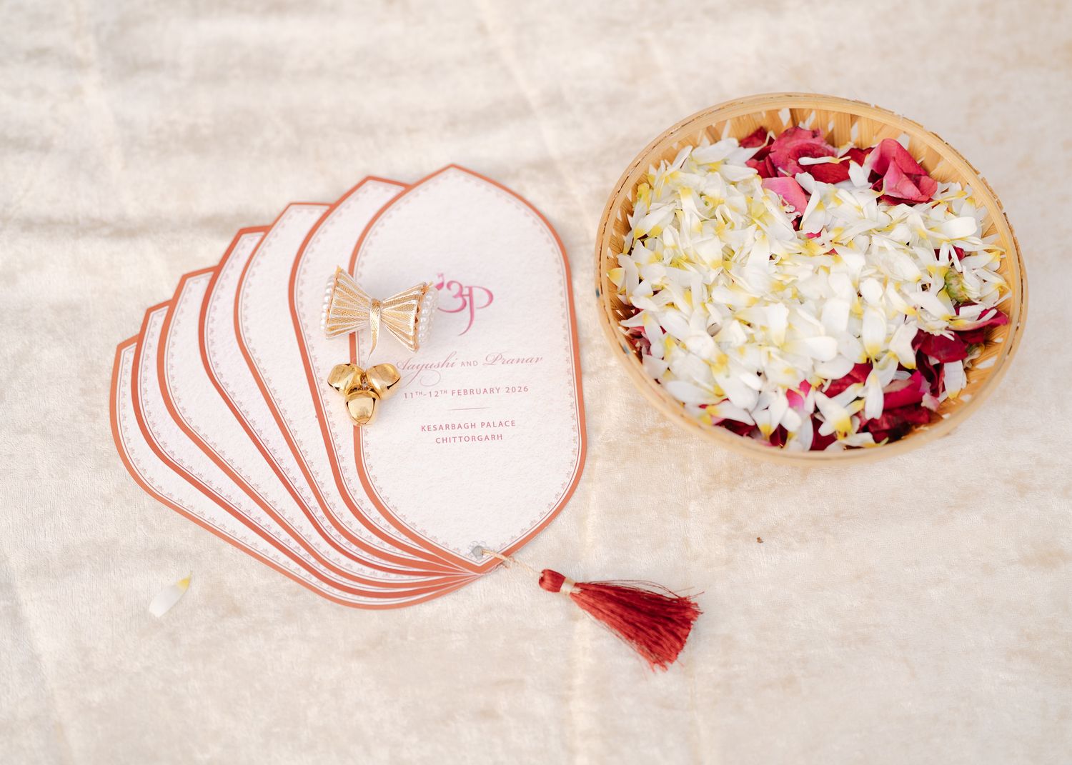 Wedding invitation cards with red tassel beside a bowl of white and red flower petals.