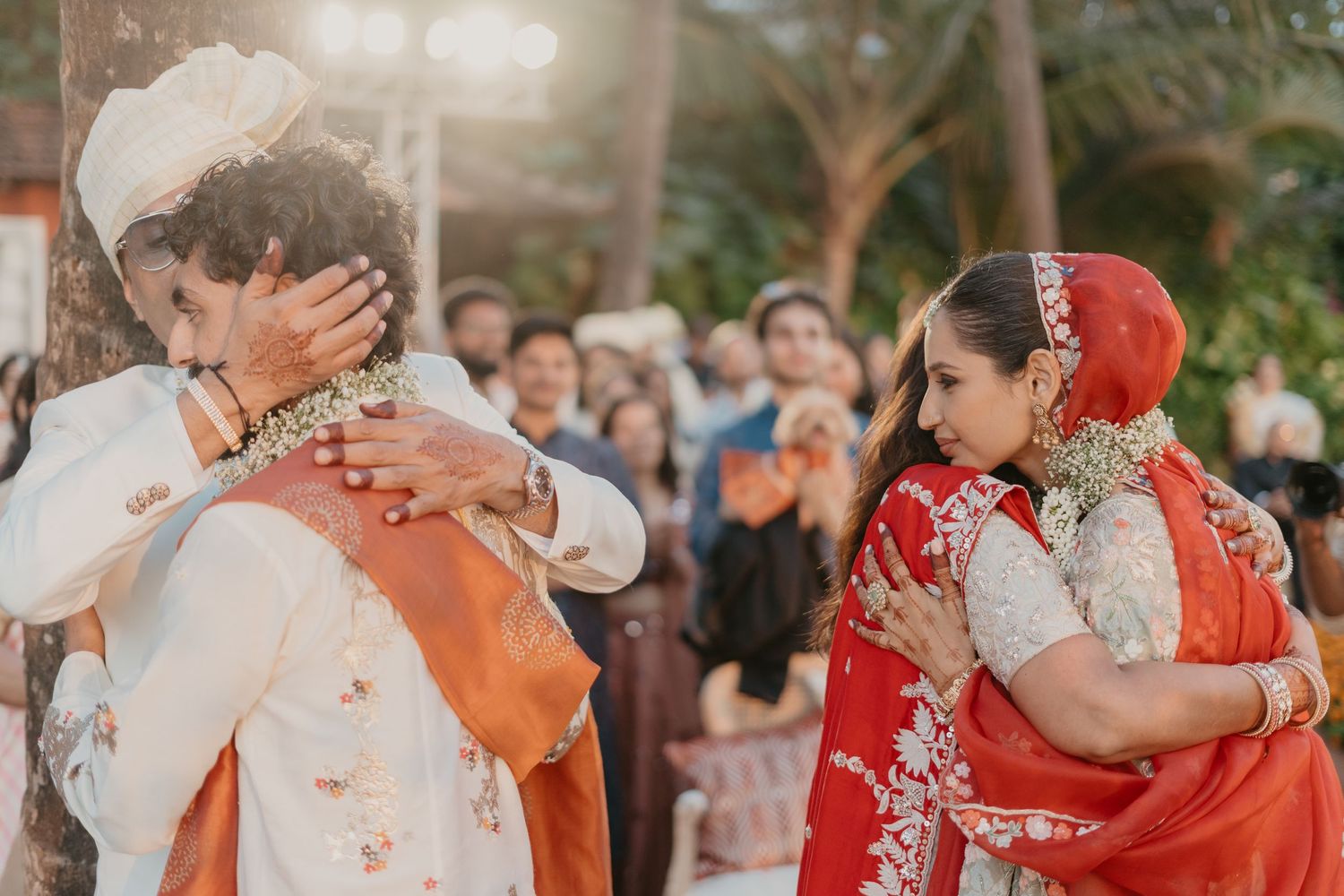Couple embracing during traditional Indian wedding ceremony outdoors, bride in red saree, groom in white sherwani.