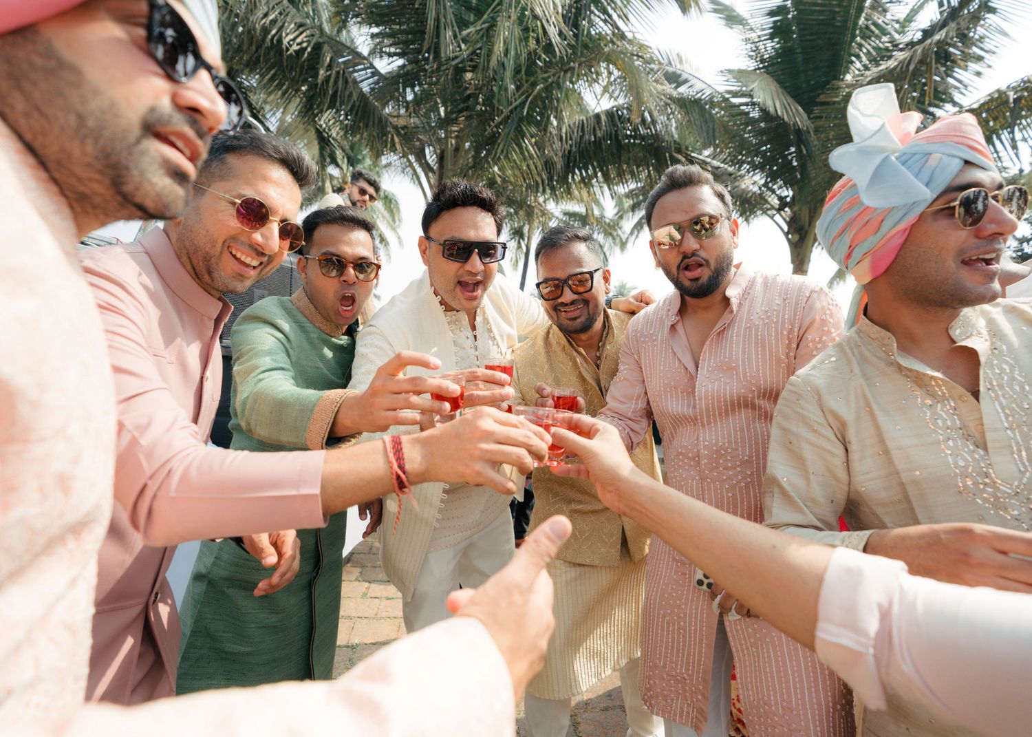 A group wearing casual summer attire is gathered outdoors under palm trees for a daytime social event.