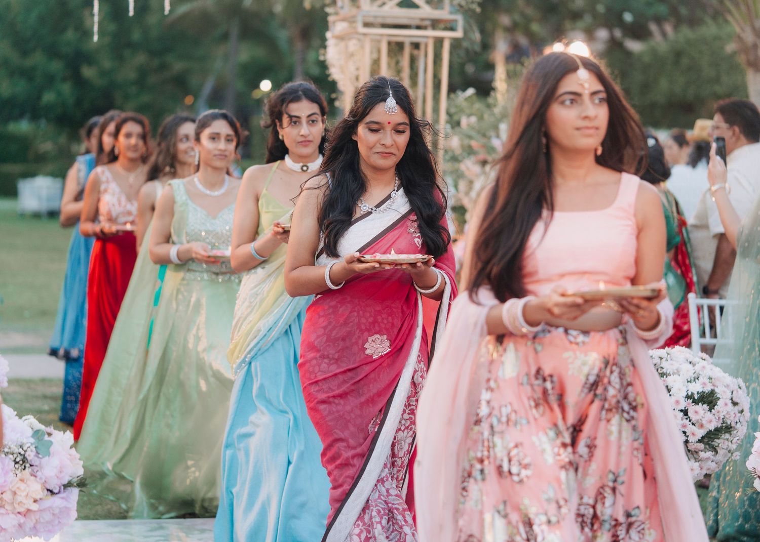 Guests in colorful traditional Indian saris and formal attire gather at an outdoor celebration event.