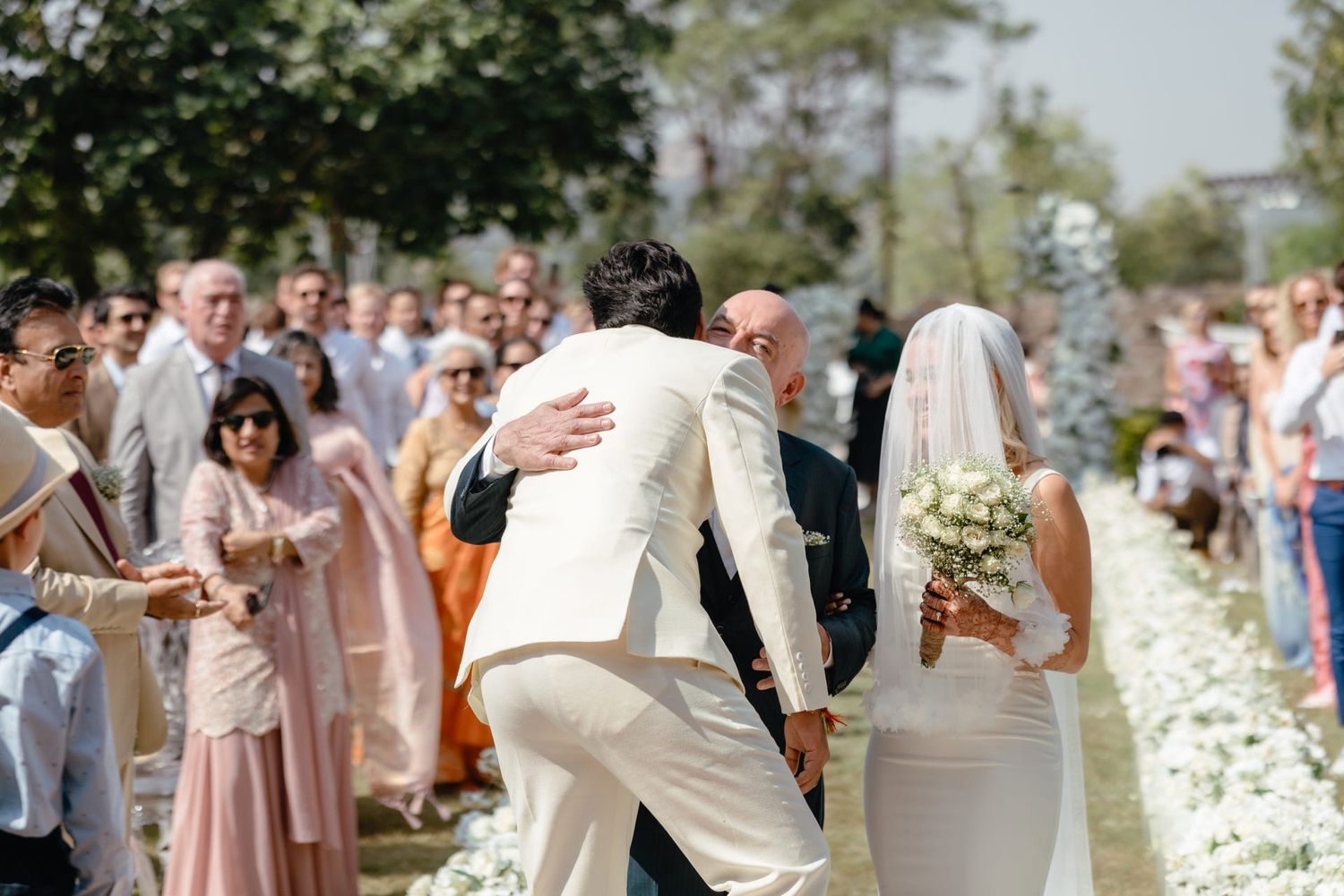 Outdoor wedding celebration with guests in pastel attire and floral decorations.