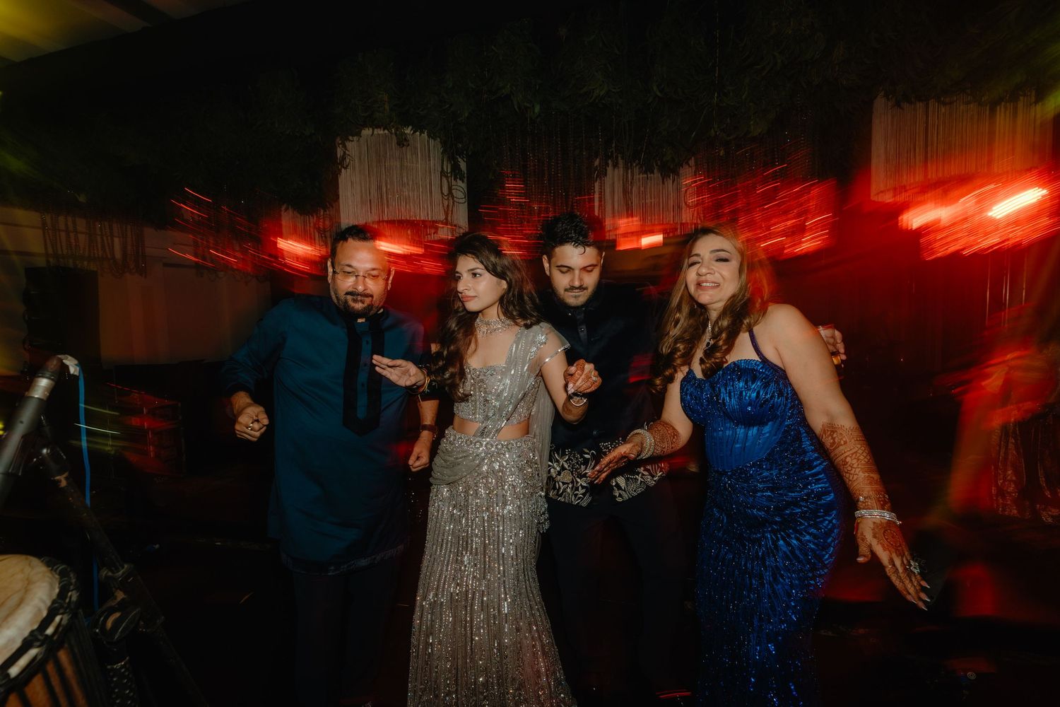 People dancing and celebrating at a dimly lit party with red lighting effects.