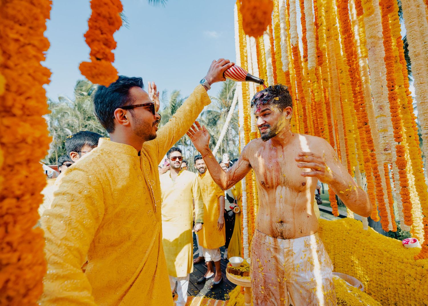 Festive wedding celebration with marigold decorations and guests throwing yellow petals in joyful celebration.