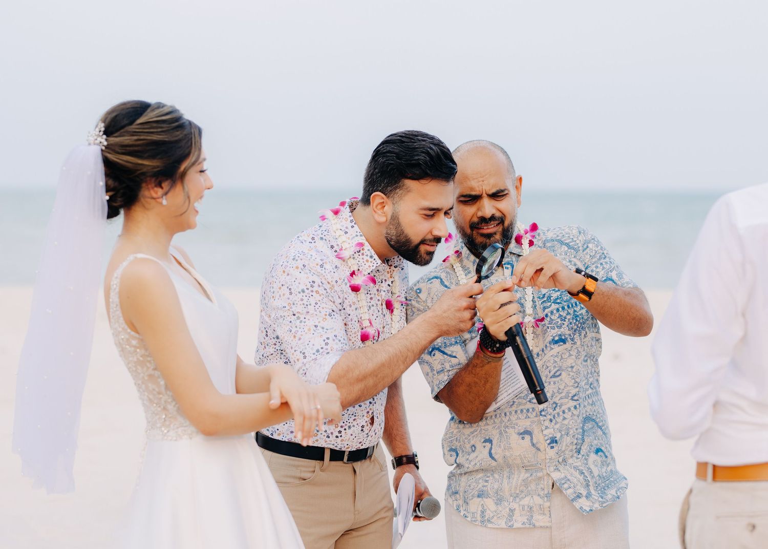 Three people share a joyful moment with microphones during a beachside celebration.