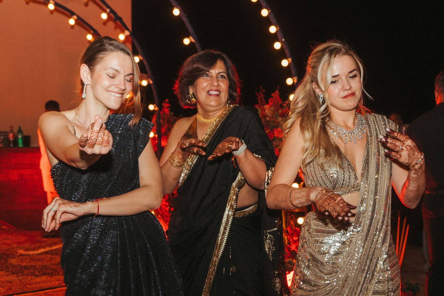 Wedding guests dancing and celebrating on a dance floor with red ambient lighting.