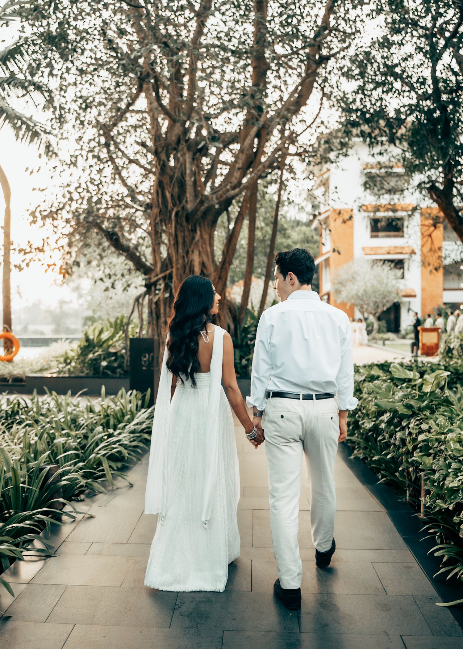 Wedding party walking along a tree-lined pathway in white formal attire.