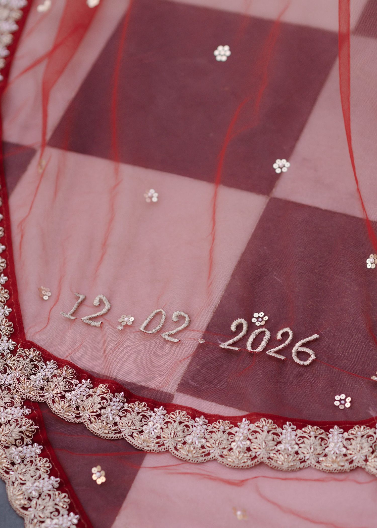 Close-up of red and pink Indian bridal dupatta embroidered with date 12-02-2026 and floral details.