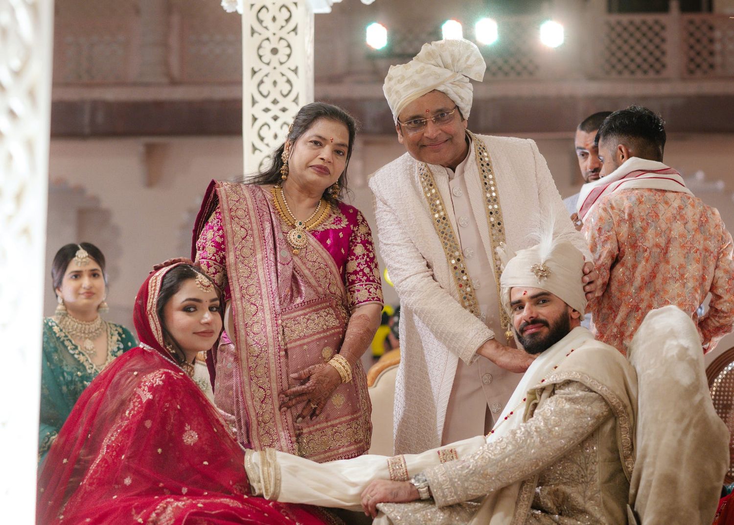 Sikh wedding ceremony with bride in red lehenga and groom in white sherwani exchanging vows with family.