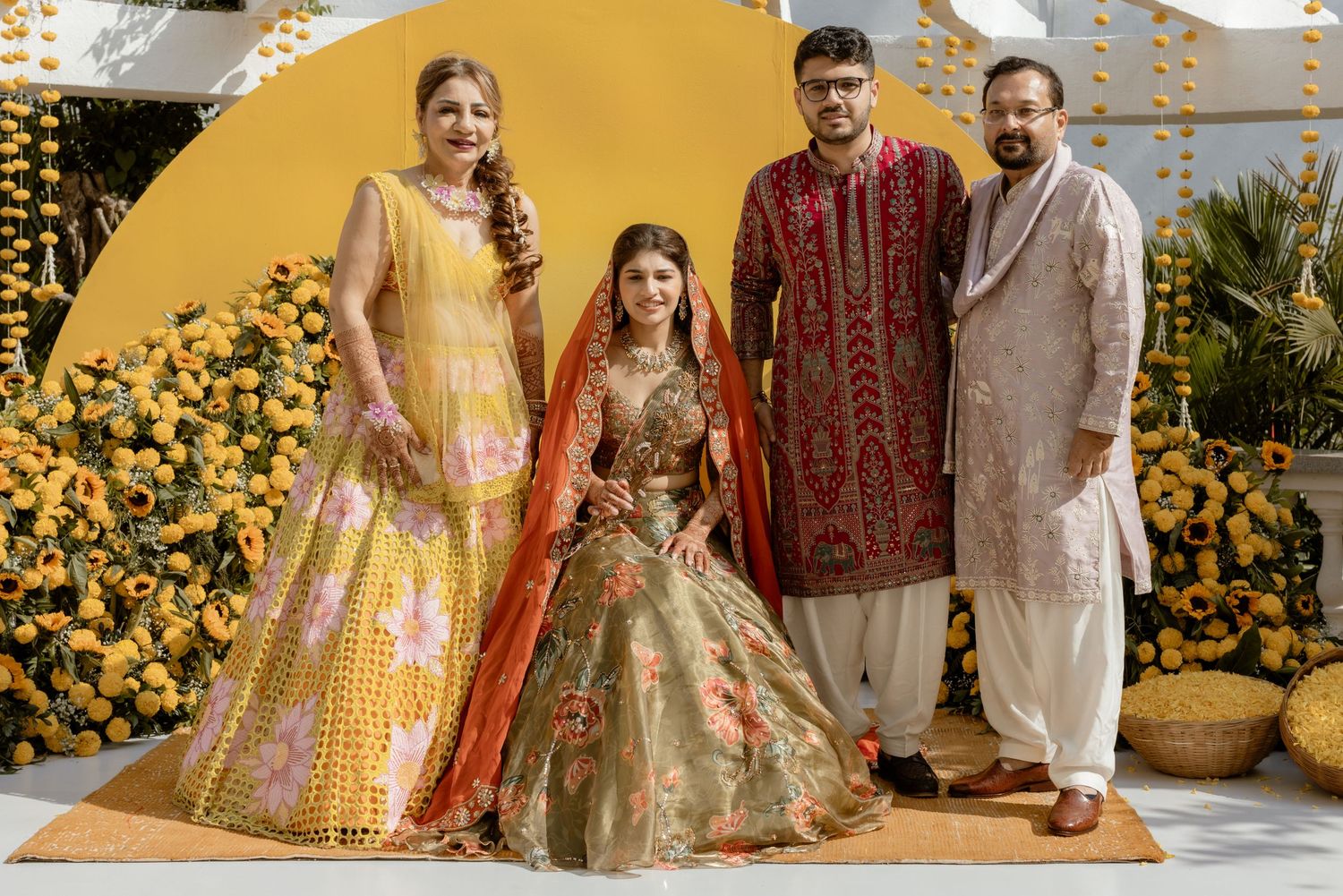 Traditional Indian wedding party poses in elegant lehengas and sherwanis against a backdrop of yellow sunflowers.