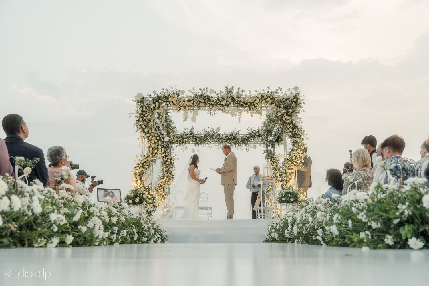 An outdoor wedding ceremony setup with floral arrangements and guests in attendance.