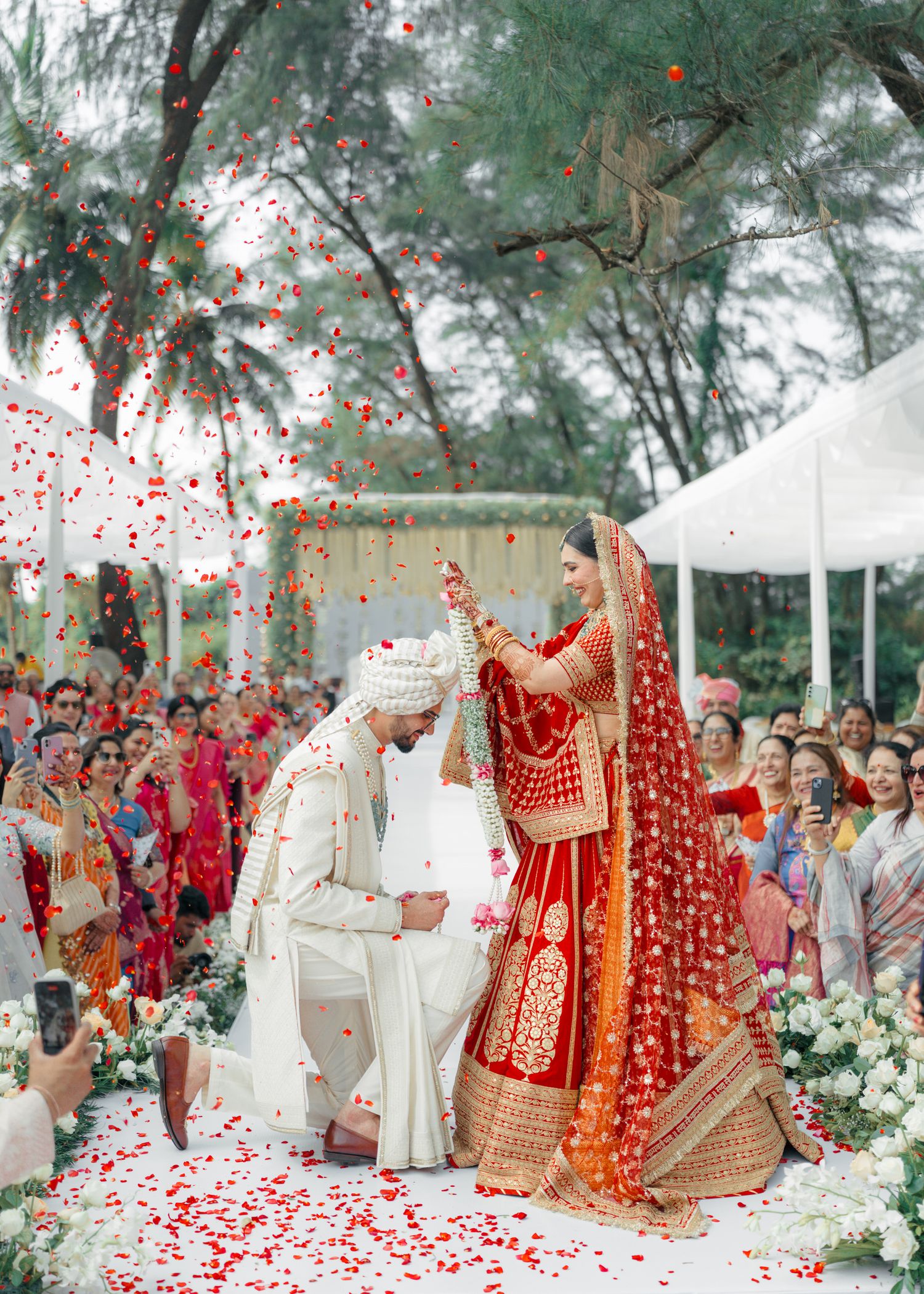 Traditional Indian wedding ceremony with red and white decorations and flower petals falling.