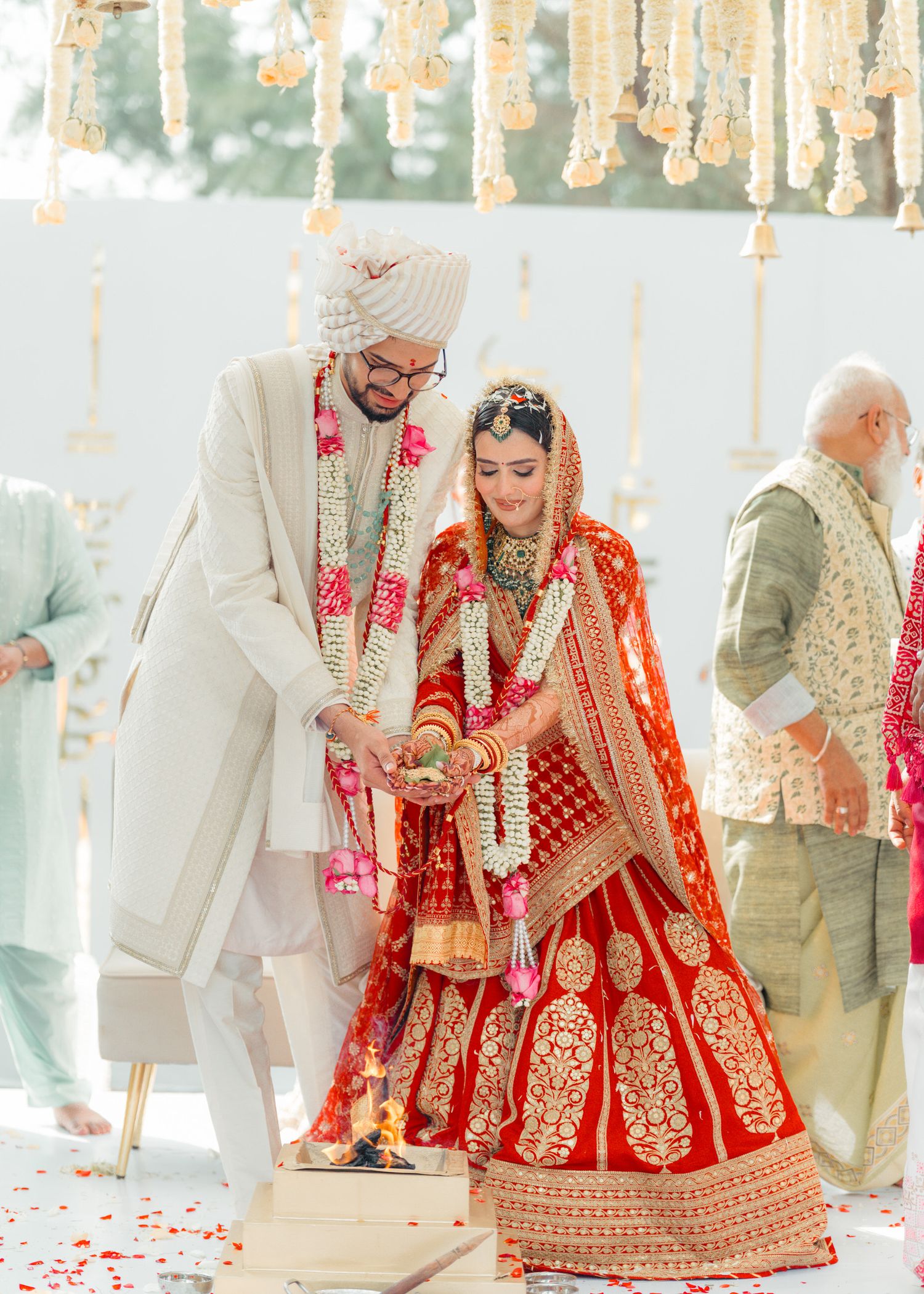 A traditional Indian wedding ceremony with the couple wearing ornate red and white attire under decorative hanging lights.