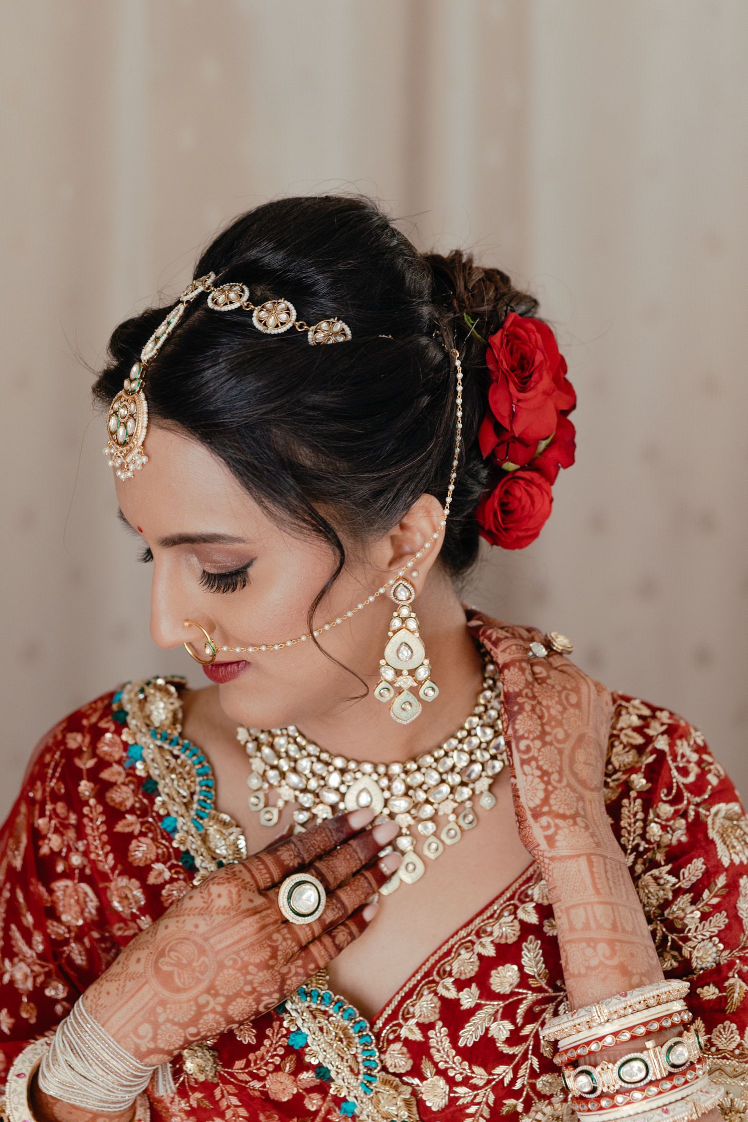 Indian bridal portrait showing traditional wedding jewelry and red attire with floral hair accessories and henna-adorned hands.