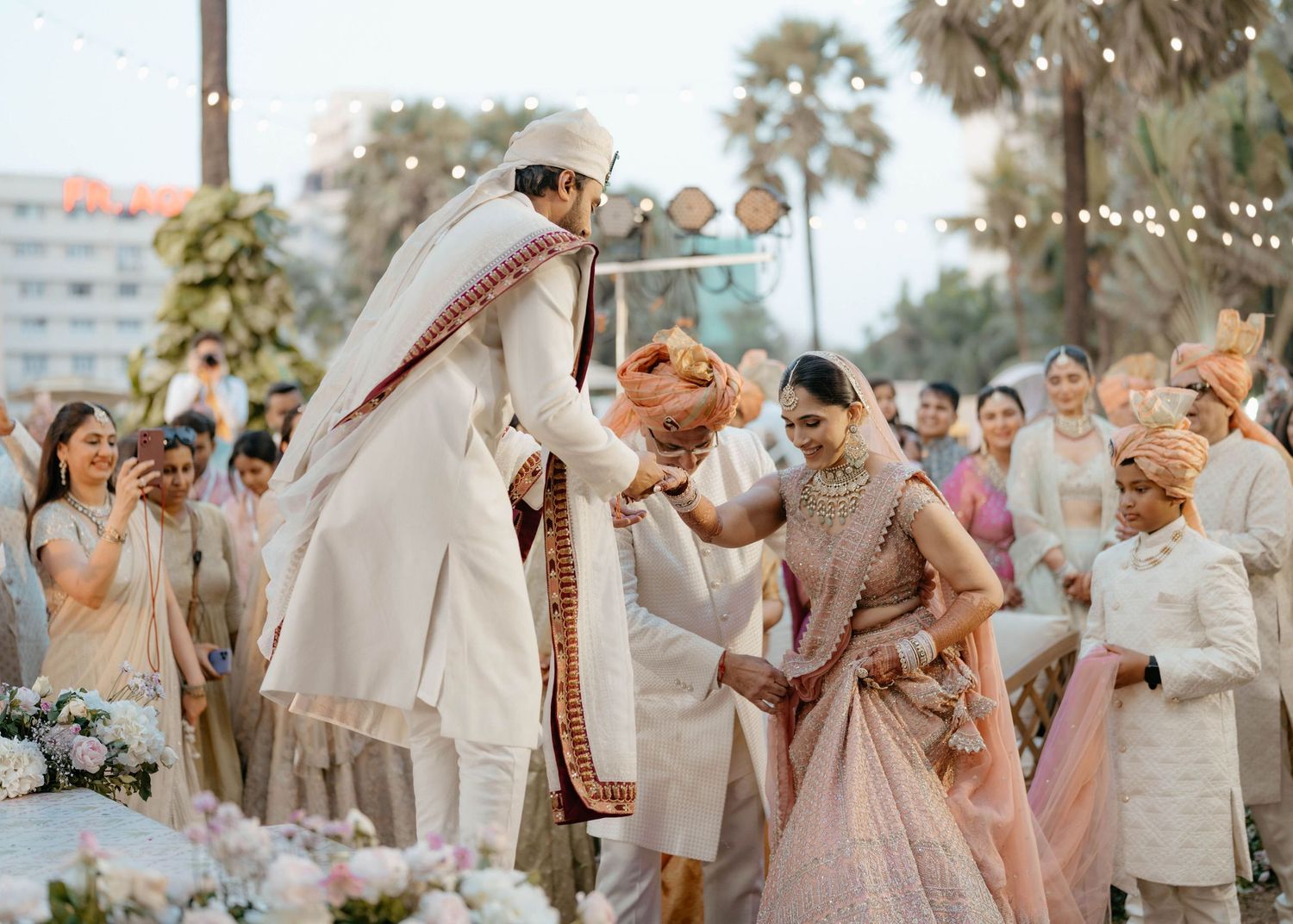 Traditional Indian wedding ceremony taking place outdoors with attendees gathered around in formal attire.