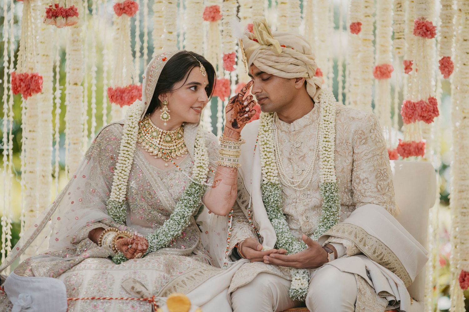 Couple in traditional Pakistani wedding attire sit together during a cultural ceremony with floral decor.