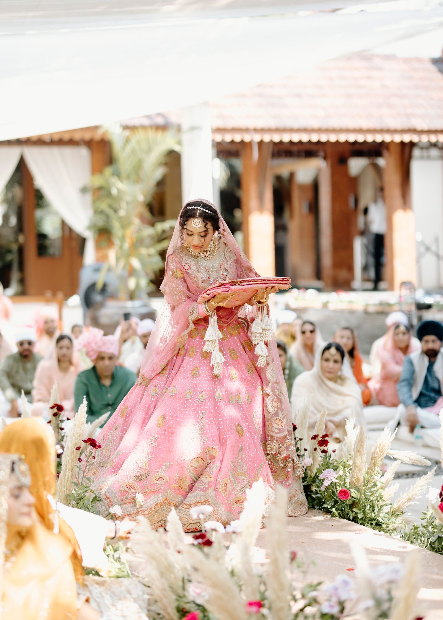 Elegant outdoor wedding ceremony with pink decor and traditional Indian elements.