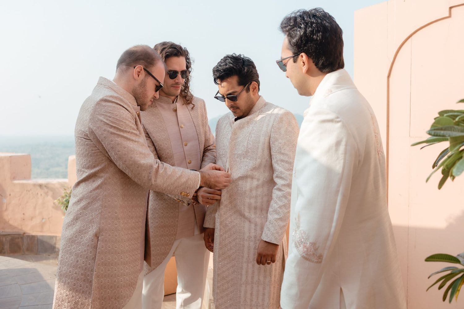 Groomsmen in cream colored traditional Indian attire sharing a lighthearted moment.