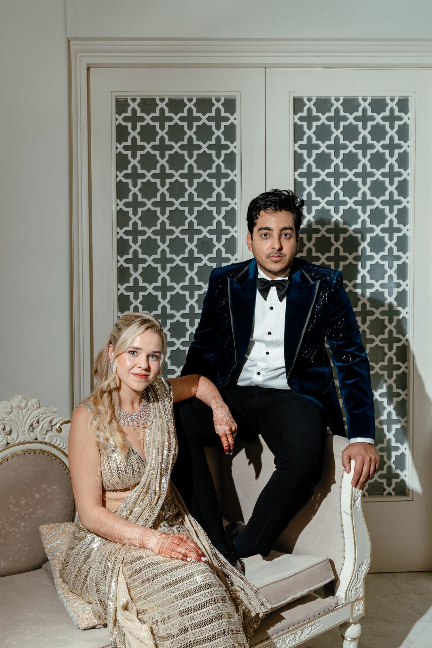 Elegant couple posing in formal attire against decorative white lattice wall panels.