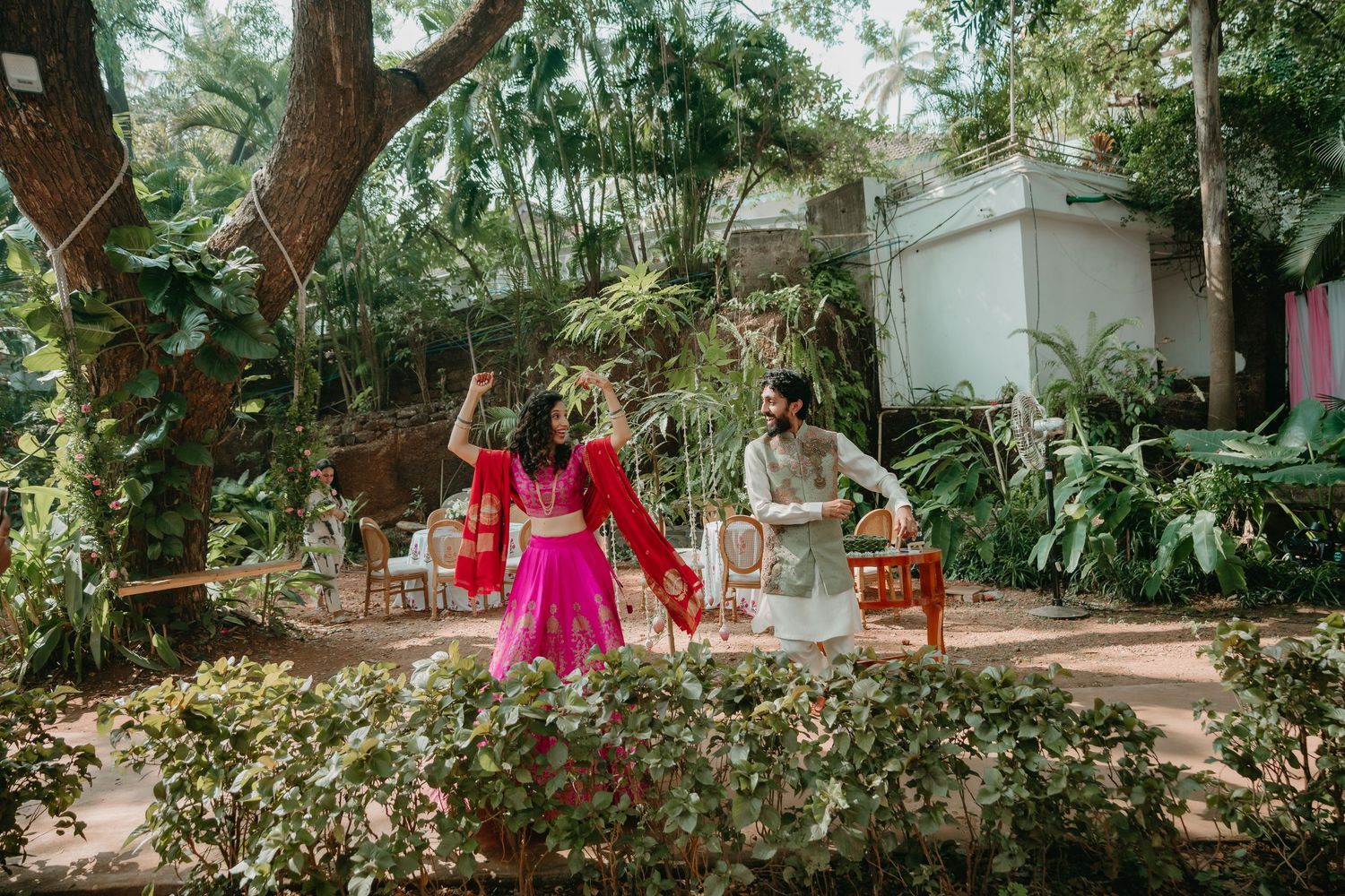 Indian couple in traditional attire dancing outdoors in a lush garden setting during a wedding celebration.