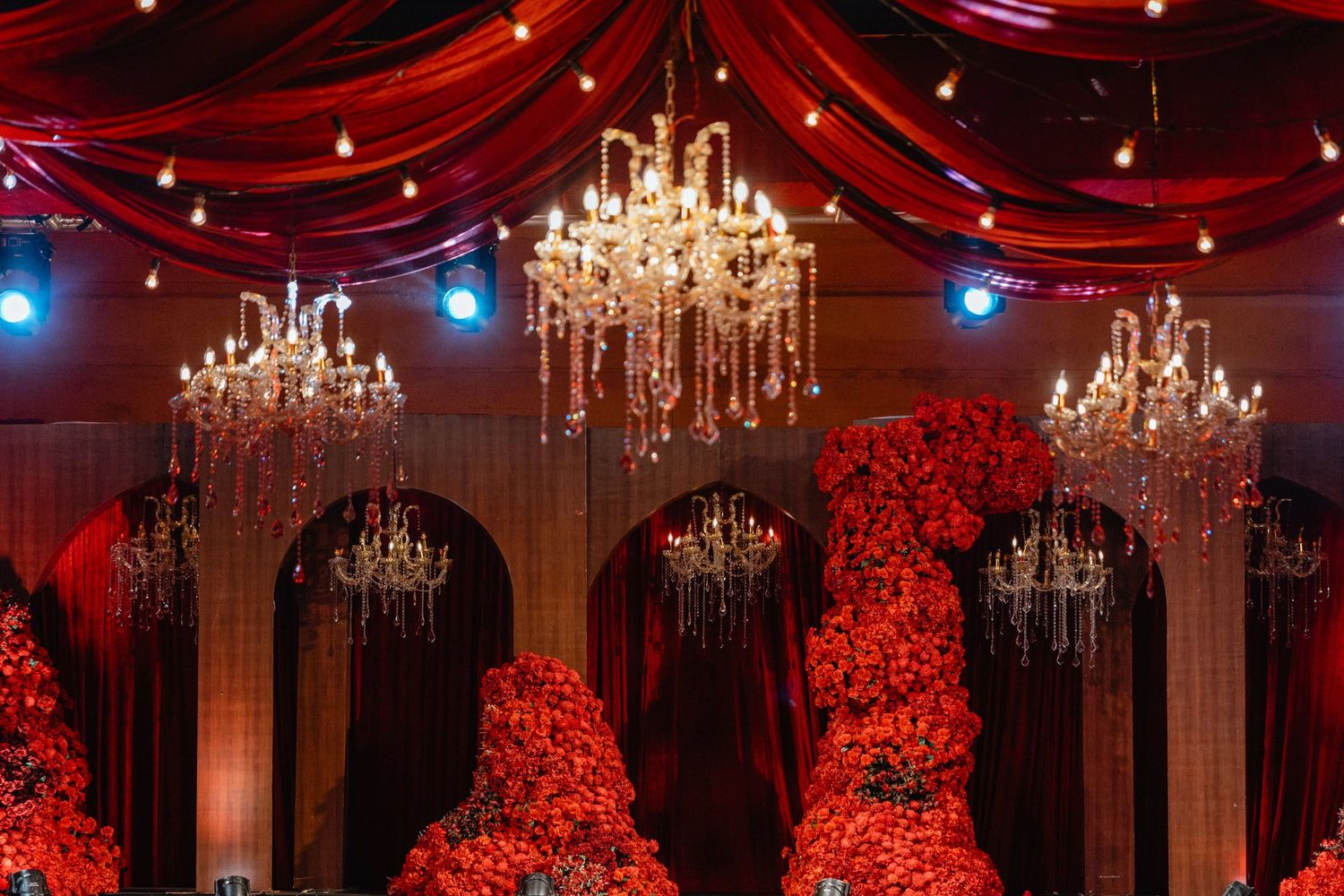 Elegant event venue with red draping, crystal chandeliers, and lush red floral arrangements creating a luxurious atmosphere.