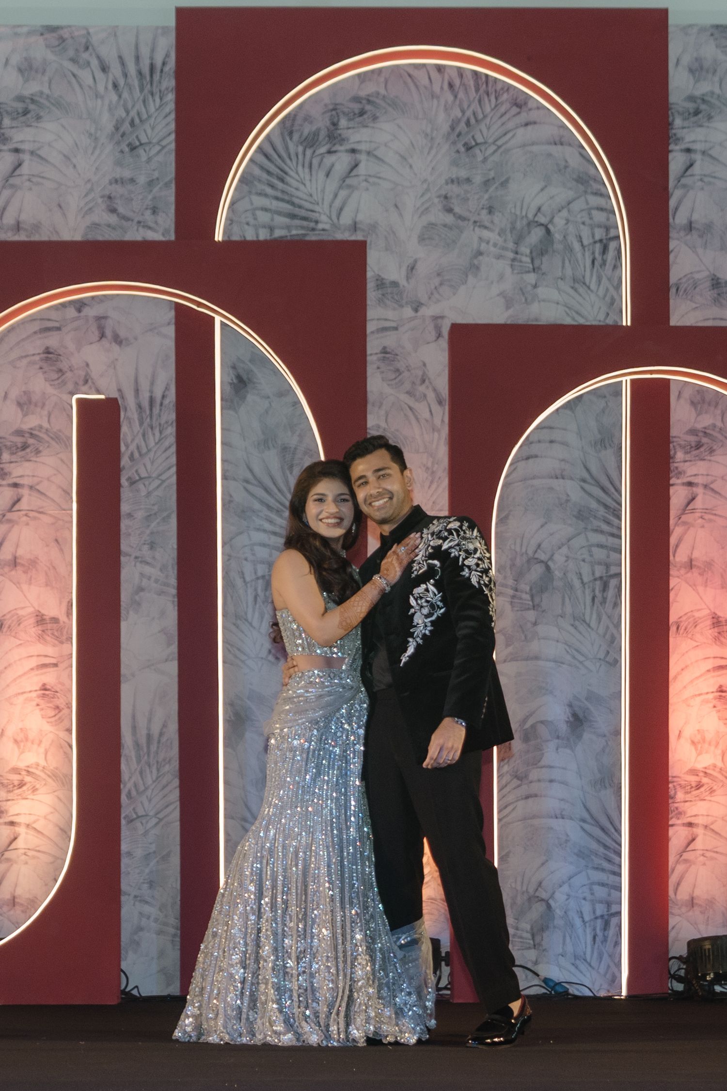 Two performers on stage with sparkly silver dress and black outfit against a burgundy and white backdrop.