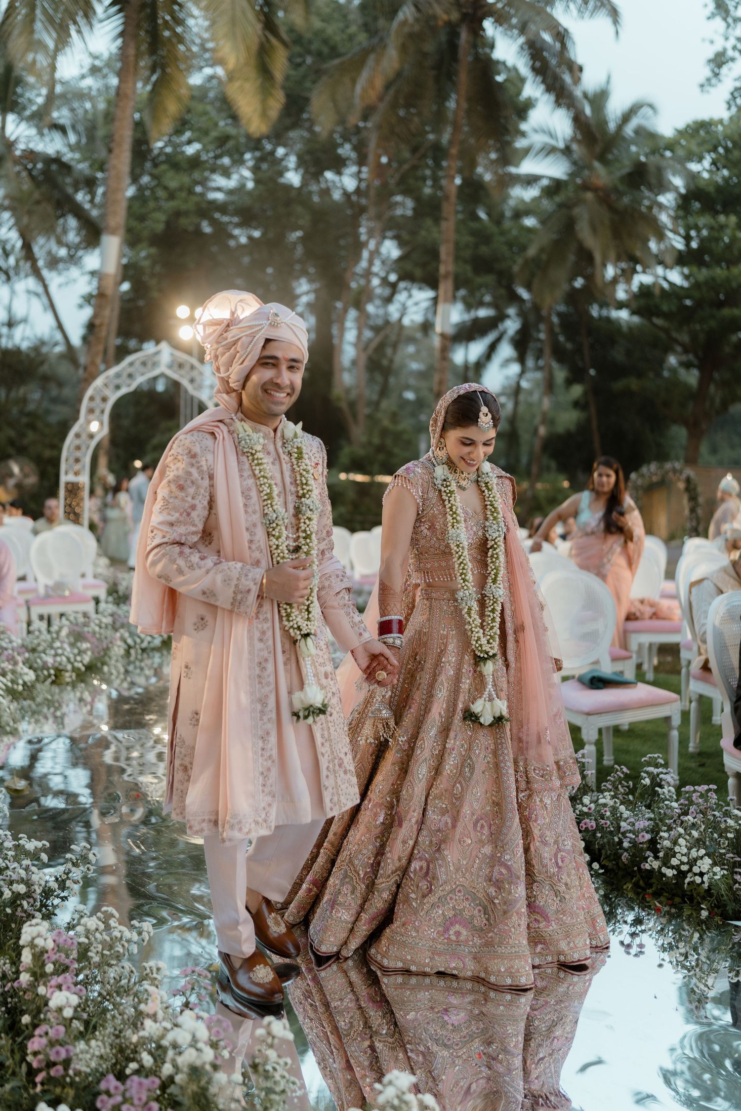 Outdoor Indian wedding ceremony setup with palm trees and white floral decorations at sunset.