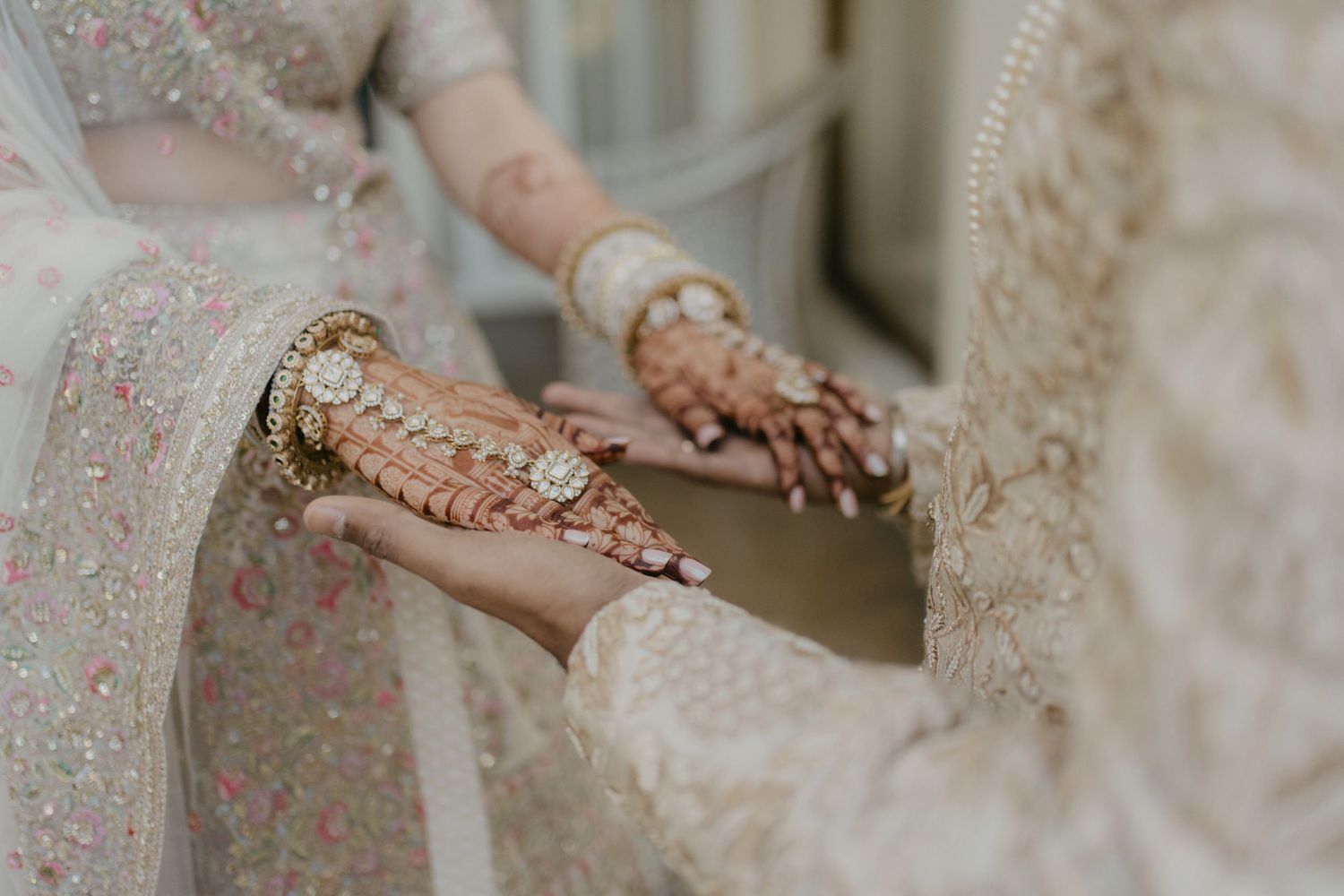 Close-up of delicate henna design being applied to hands with traditional bridal jewelry.