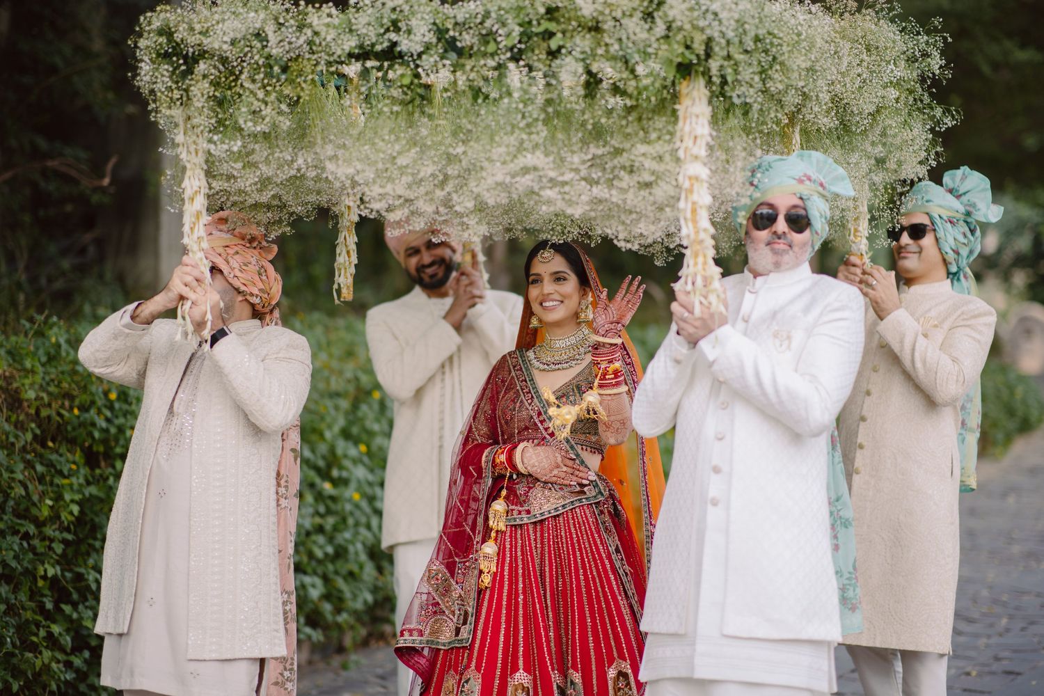 Wedding party in cream colored outfits and red dress share emotional reactions during outdoor ceremony.