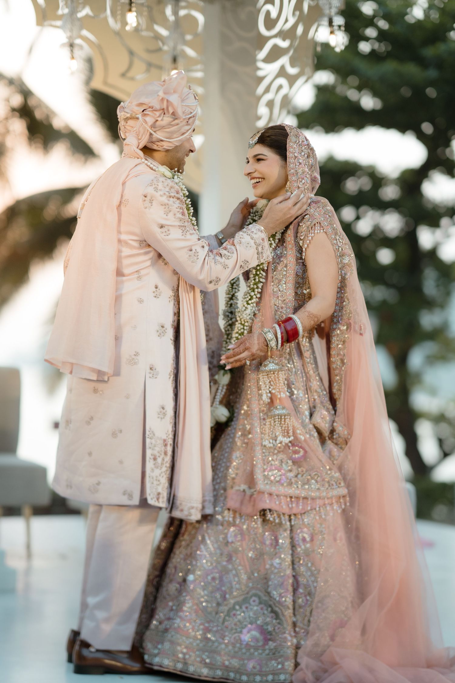 Ornate pink bridal outfits with intricate embroidery and sequin work shown in outdoor garden setting.