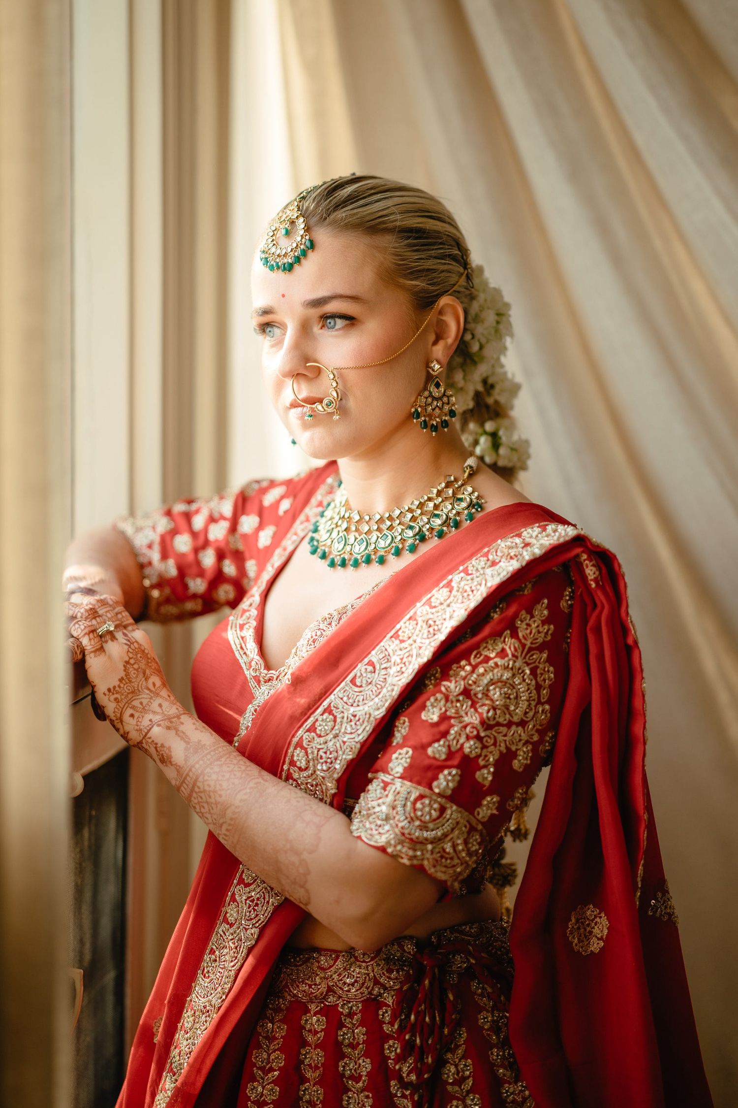 Elegant bride in red and gold Indian wedding attire with traditional jewelry and henna.