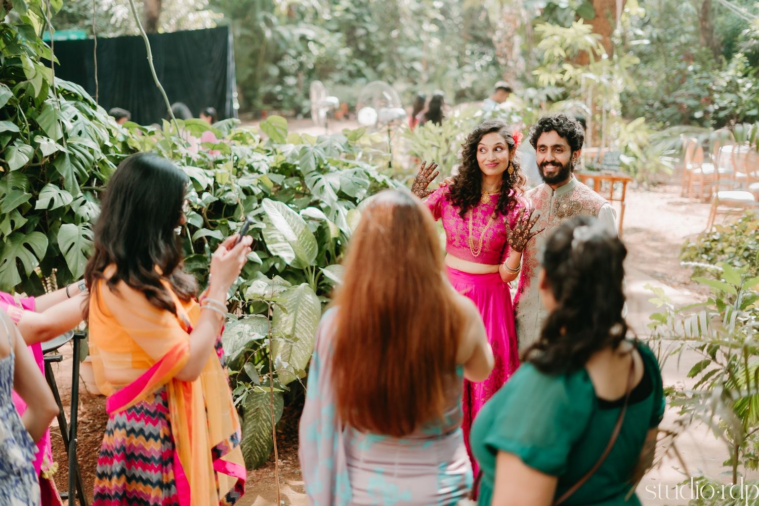 Outdoor wedding celebration with guests in vibrant traditional attire surrounded by greenery.