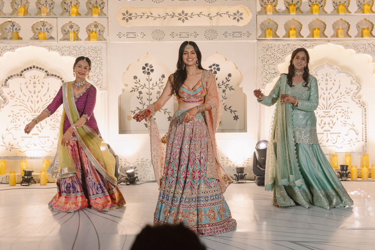 Three women showcase colorful lehengas in pink, blue and gold during an Indian wedding fashion display.